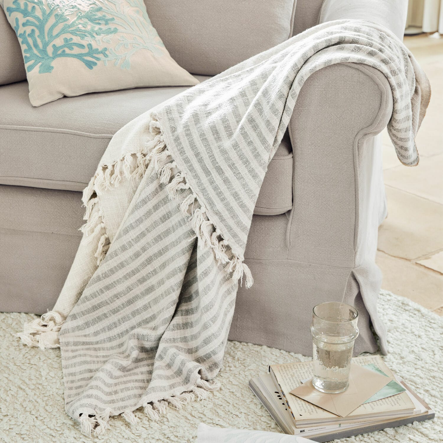Plaid Marpent Manta beige a rayas con flecos sobre sofá gris claro, accesorio acogedor para salón
