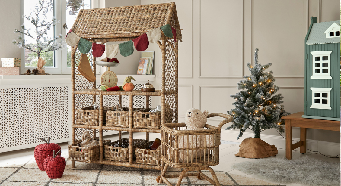 Estantería de mimbre con cestas y decoraciones en habitación acogedora con árbol de Navidad y juguetes