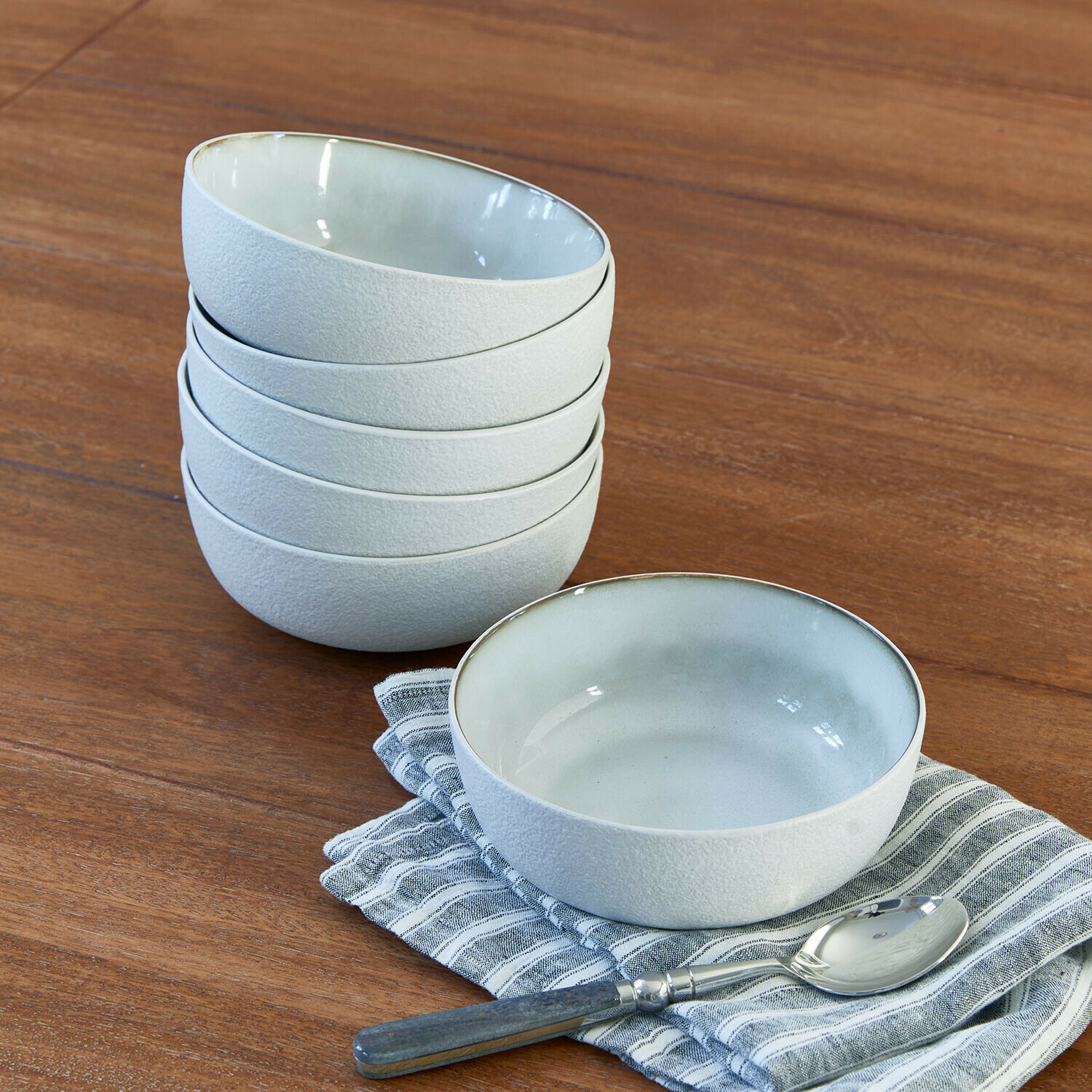 Set de 6 cuencos Eiruna Conjunto de cuencos de cerámica blanca con textura mate sobre mesa de madera con cuchara y paño