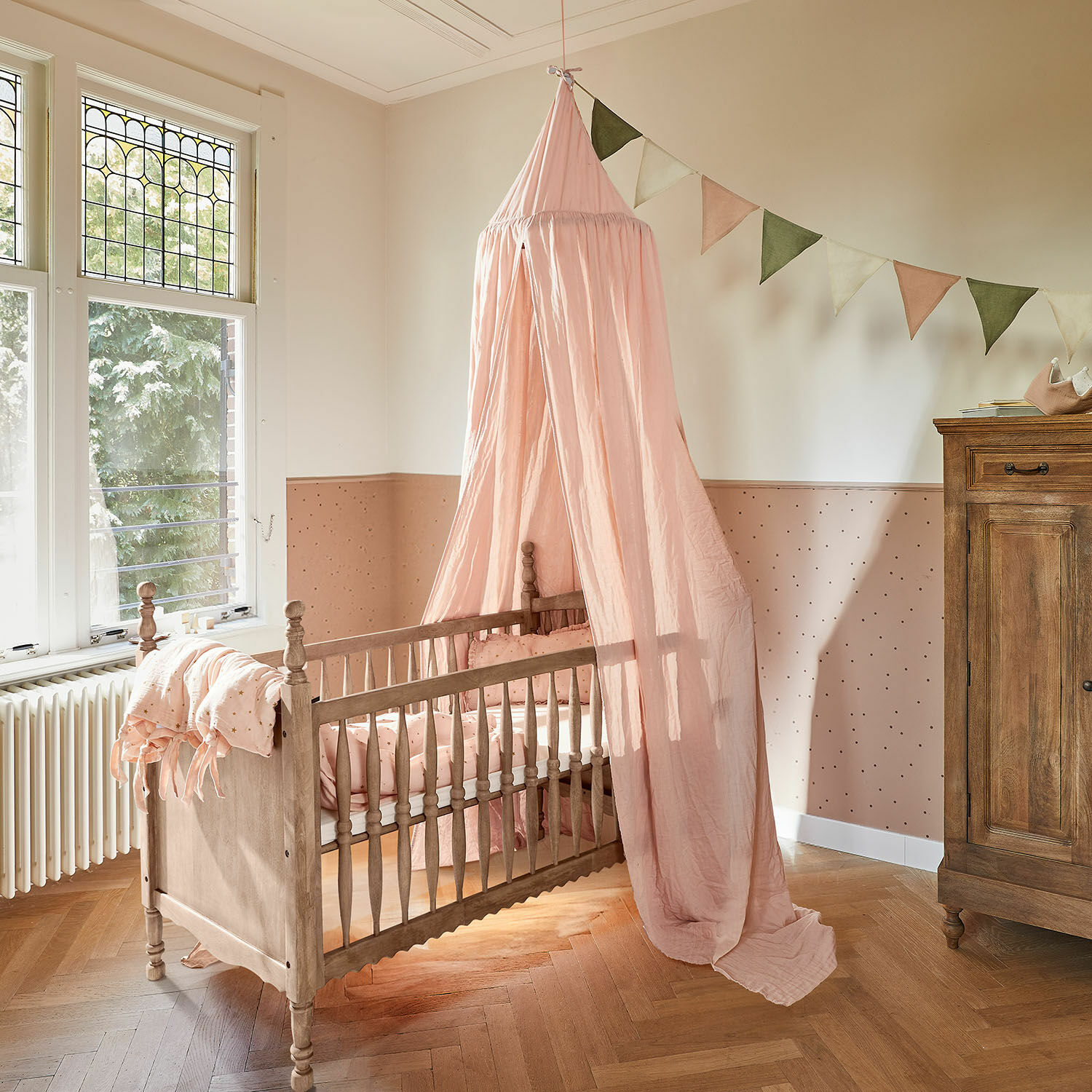 Cuna de bebé Merveillon Cuna de madera con dosel rosa y ropa de cama a juego en habitación infantil de tonos pastel
