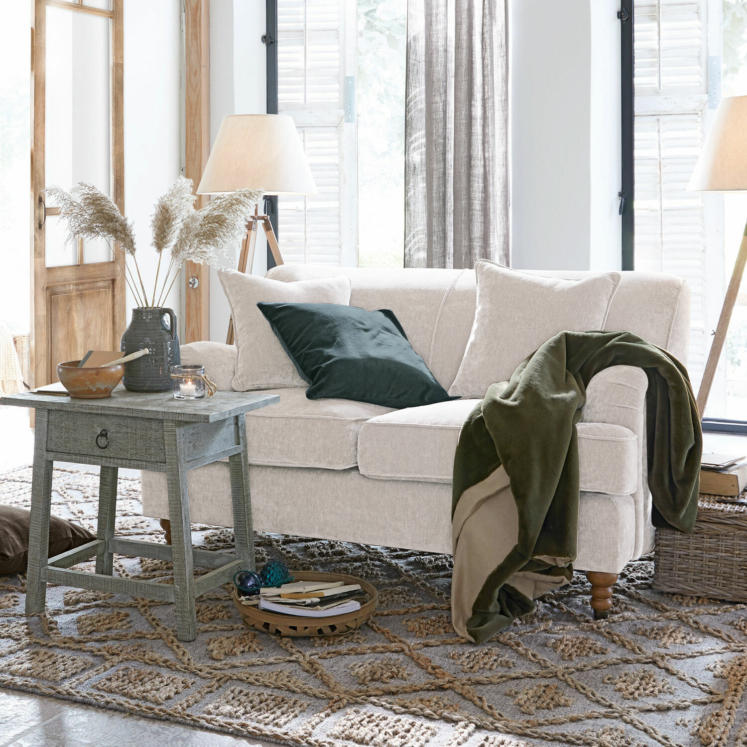 Sofá beige de tela suave con manta verde y cojín en sala acogedora con mesa de madera