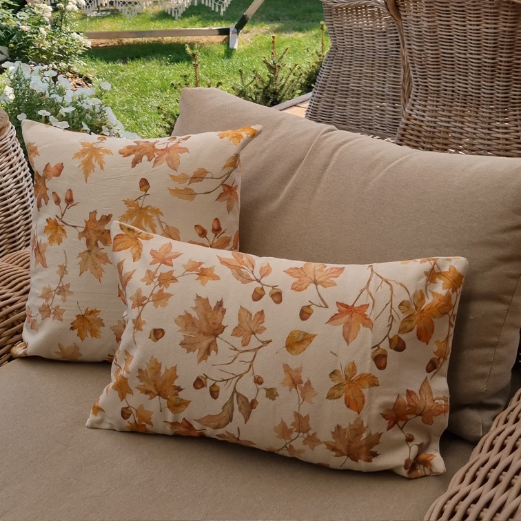 Cojines decorativos de algodón beige con estampado de hojas otoñales y bellotas en sofá de jardín de mimbre