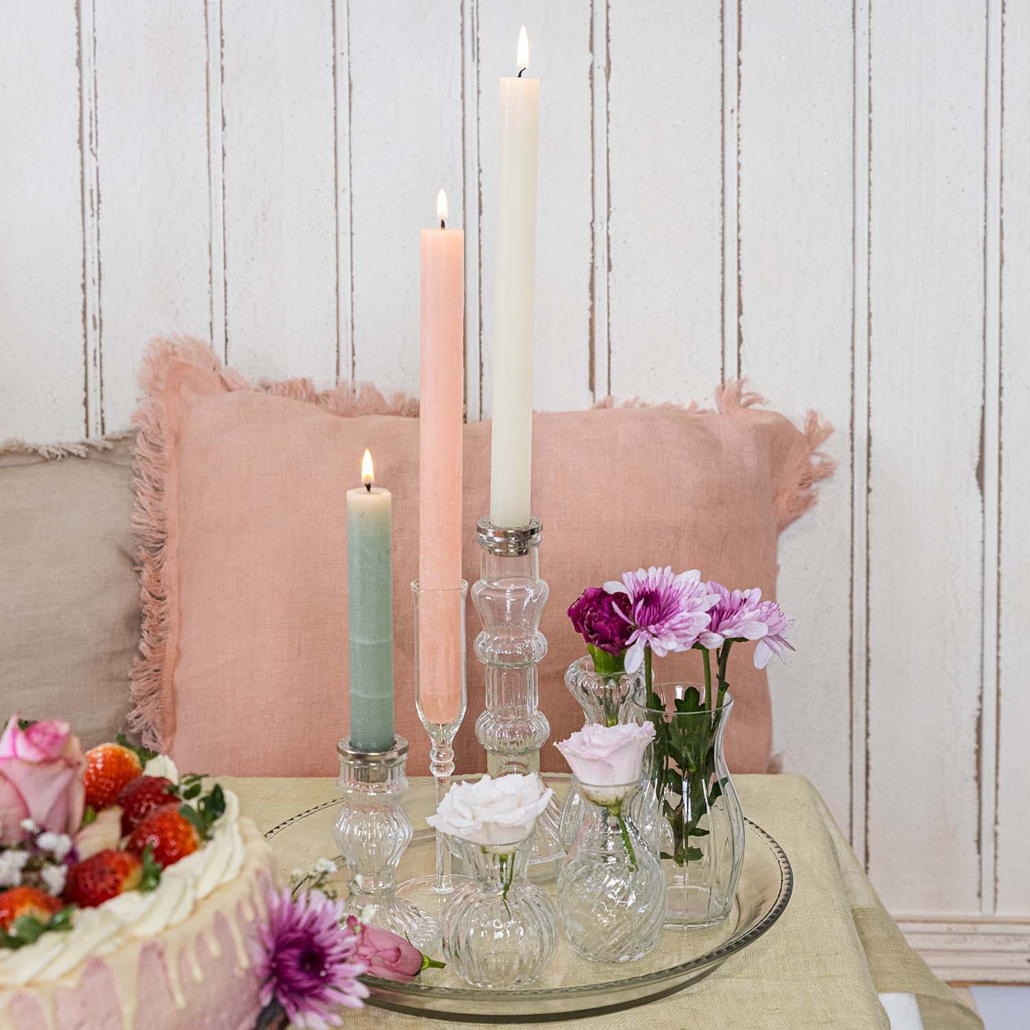 Velas en tonos pastel y pequeños jarrones de cristal con flores sobre una bandeja de cristal en la mesa