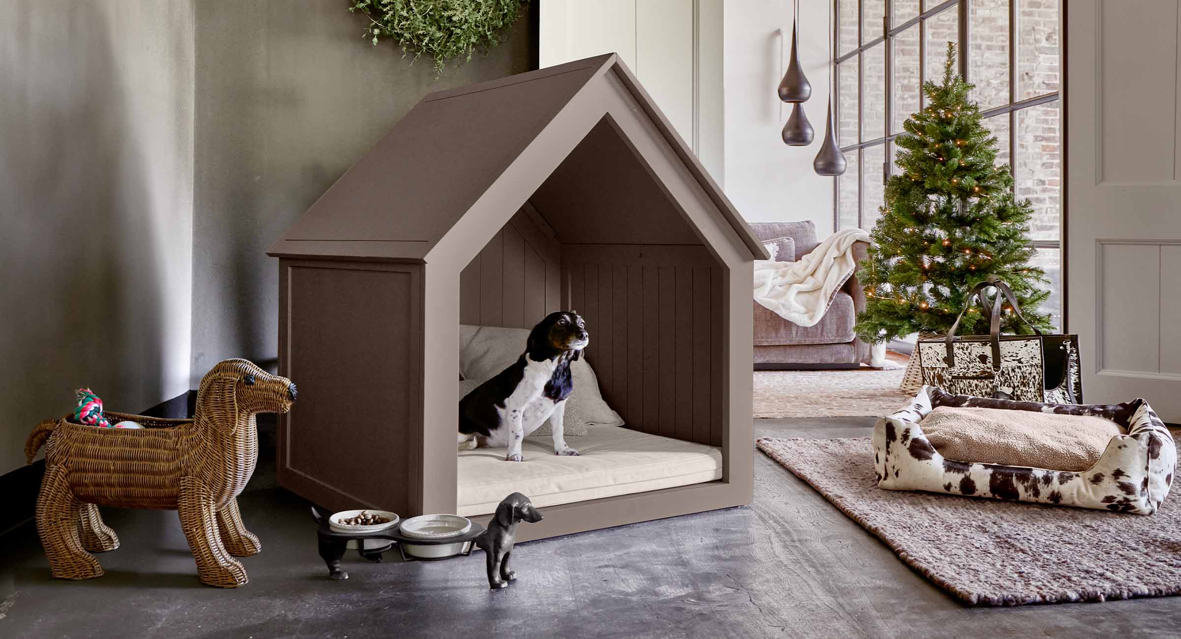 Caseta para perro de madera marrón con cojín crema en salón moderno con árbol de Navidad y juguetes