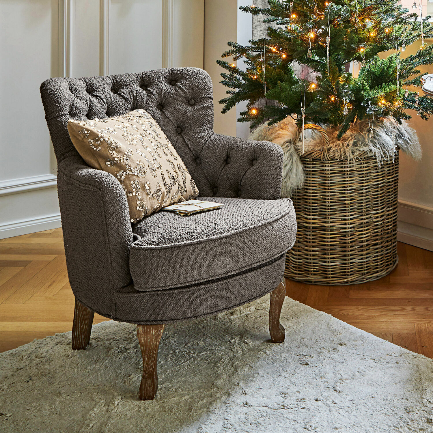 Sillón Calgary Sillón tapizado gris con patas de madera sobre alfombra clara junto a árbol de Navidad decorado