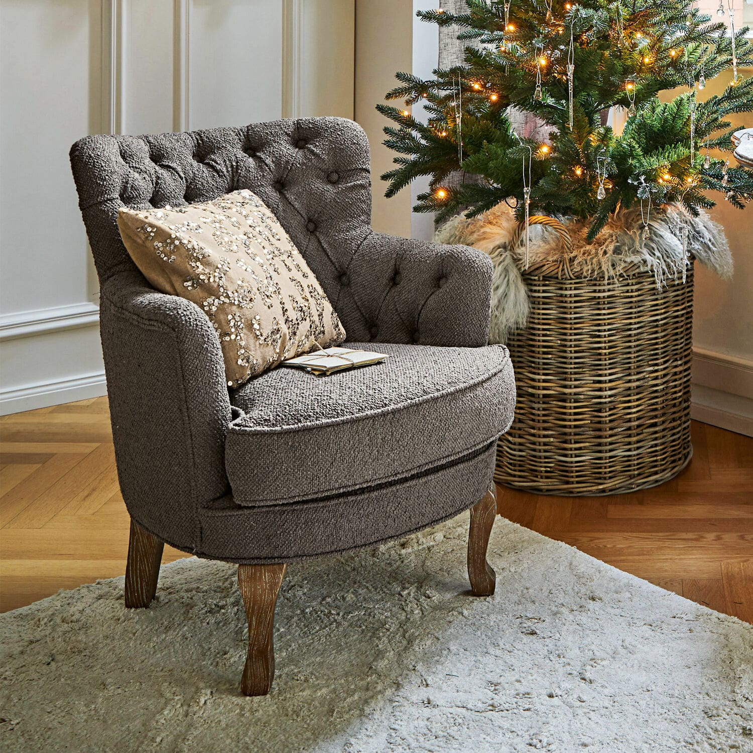 Sillón Calgary Sillón tapizado gris con patas de madera sobre alfombra clara junto a árbol de Navidad decorado