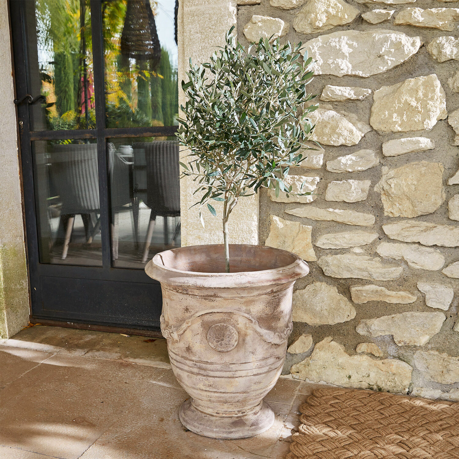Maceta Garwood Maceta grande decorativa de terracota beige con planta verde en terraza de piedra