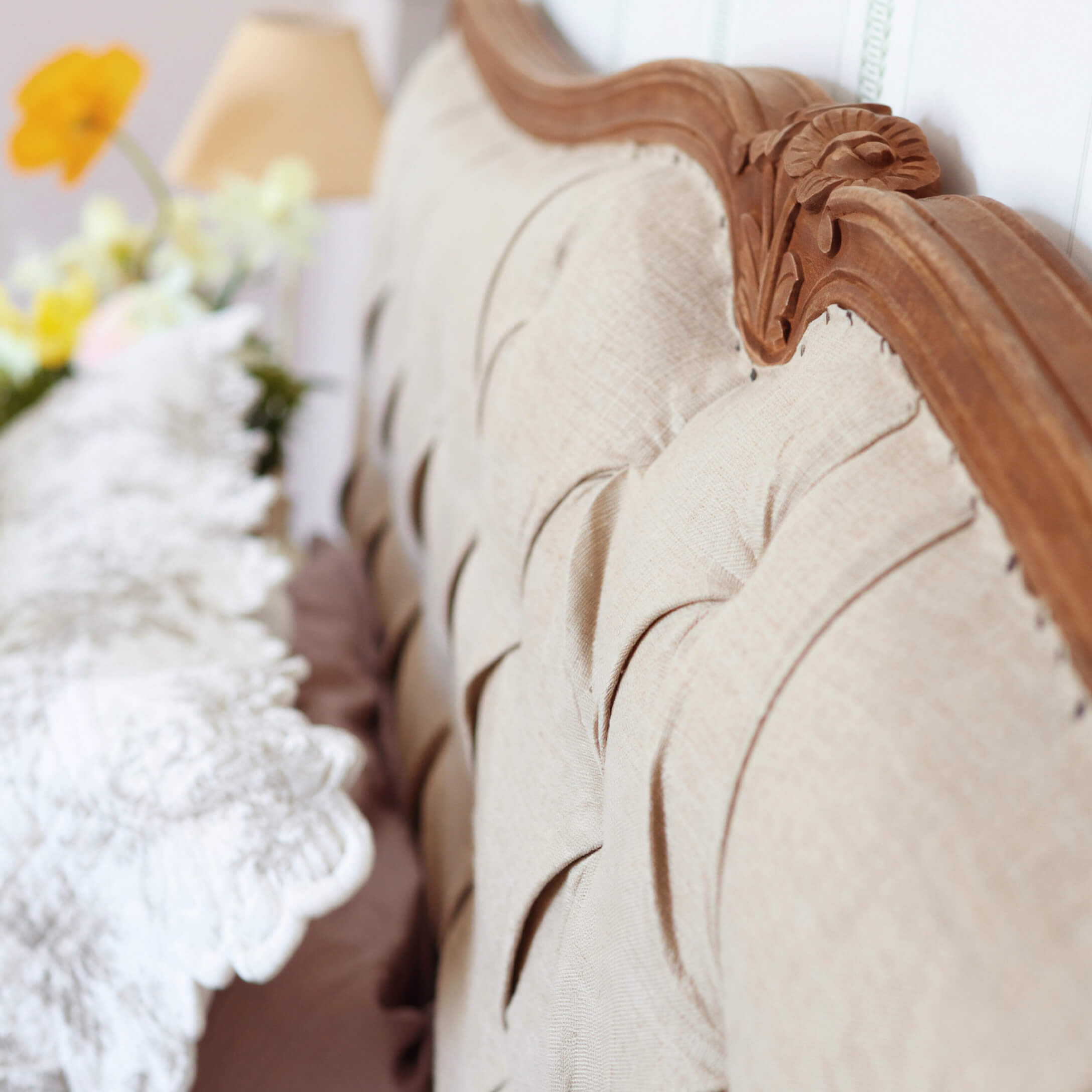 Respaldo tapizado beige con marco de madera tallada y cojín decorativo desenfocado al fondo