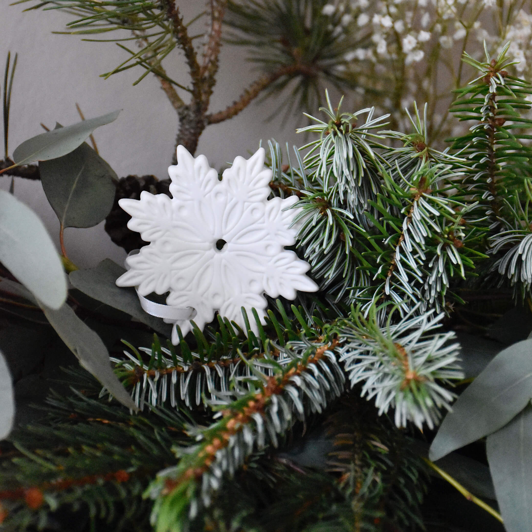 Adorno navideño de cerámica blanca en forma de copo de nieve sobre ramas verdes de abeto