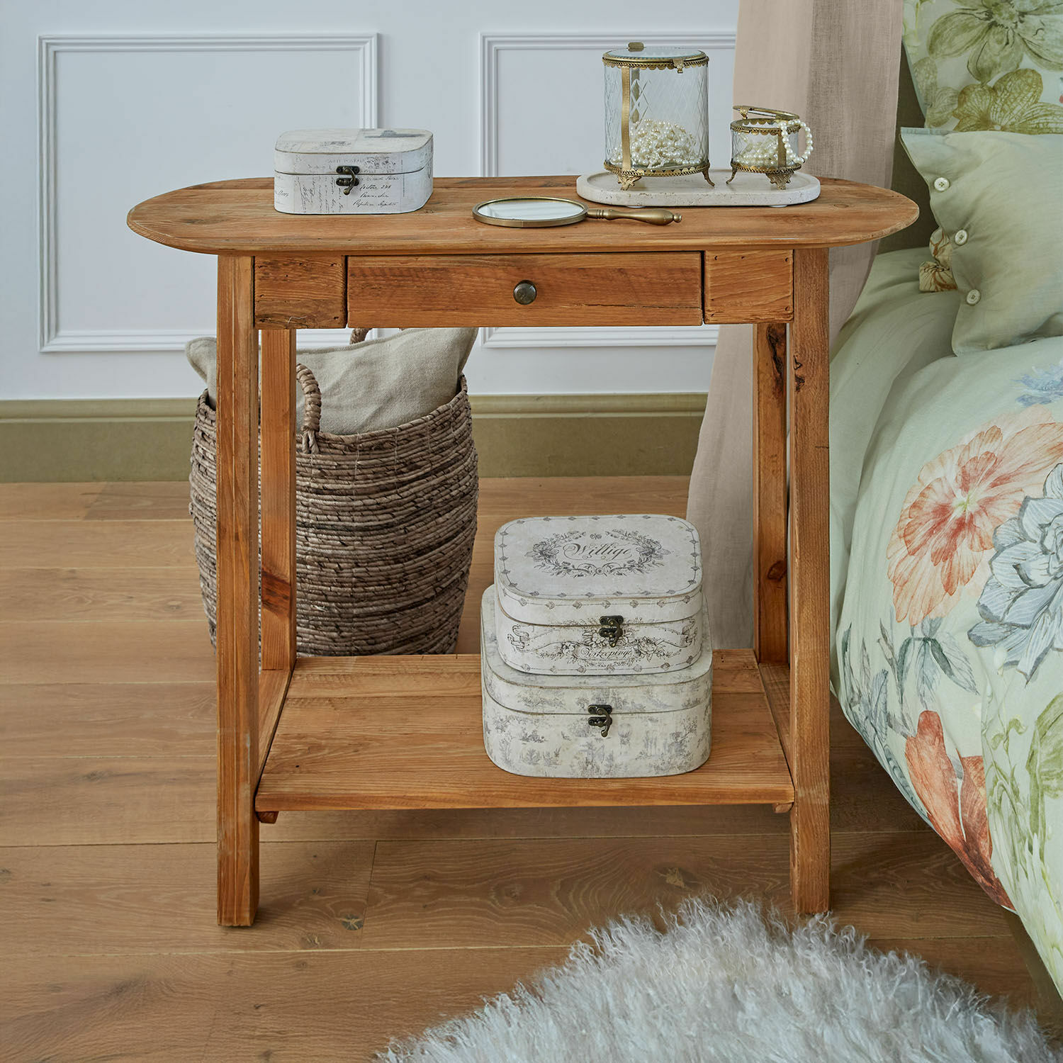 Mesita de noche de madera con cajón y cajas decorativas vintage sobre suelo de madera clara en dormitorio