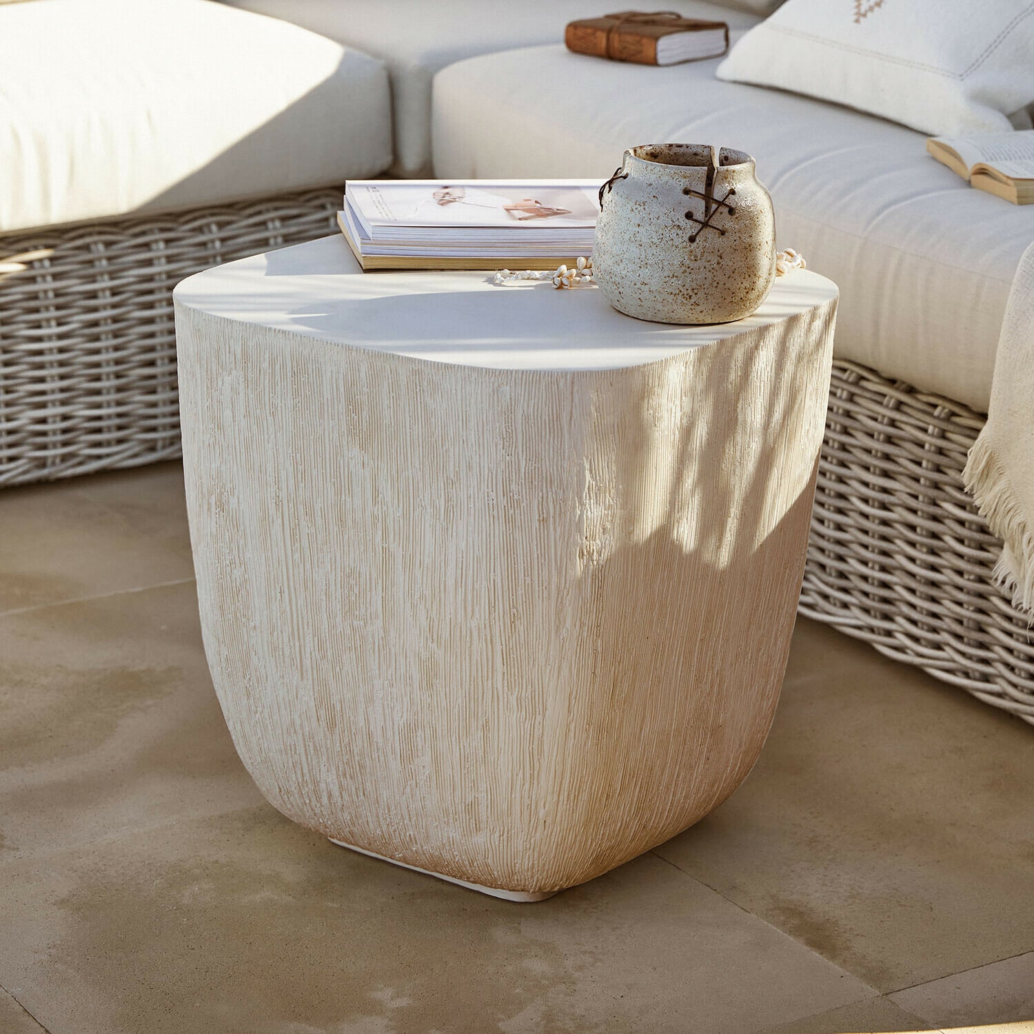 Mesa auxiliar Nélomiane Mesa auxiliar beige con textura de madera, cerámica y libros en terraza con sofá de mimbre