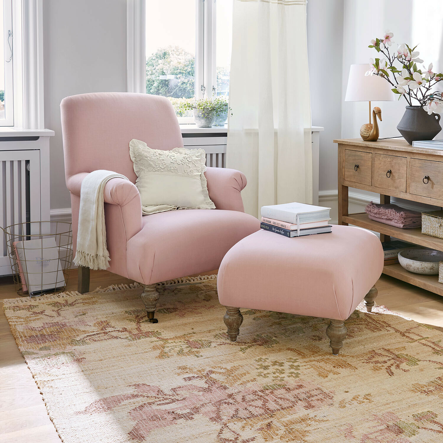 Sillón con reposapiés Rose de Lumière Sillón y reposapiés rosa de tela en salón luminoso con mesa de madera y decoración