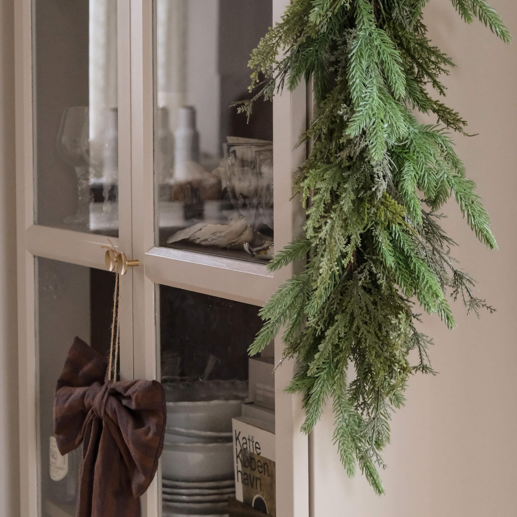 Guirnalda decorativa verde de ramas colgada en un armario claro con puertas de cristal estilo escandinavo