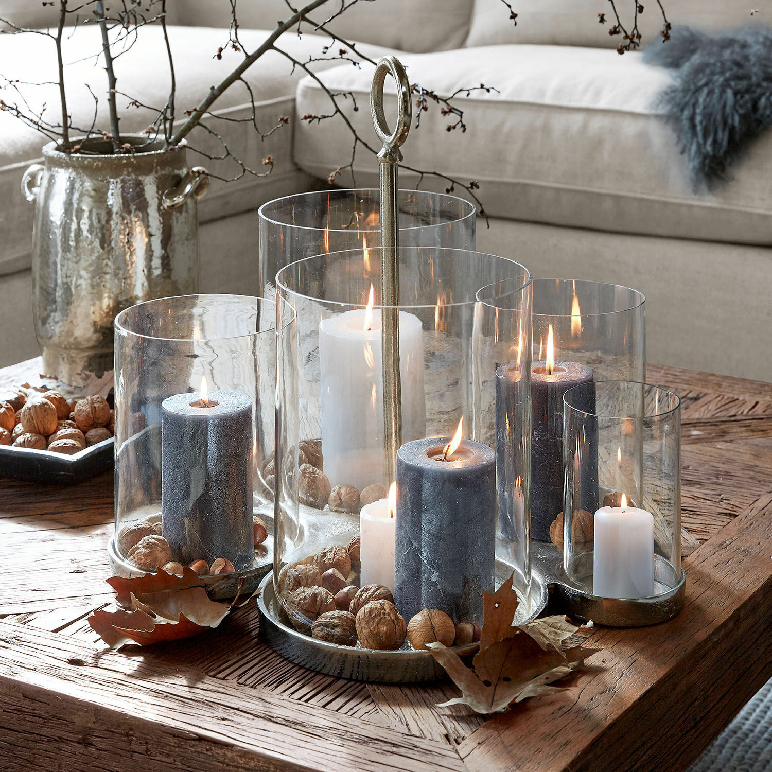 Farolillo Gjaloran Conjunto de portavelas de vidrio y metal con velas blancas y grises y nueces sobre mesa de madera