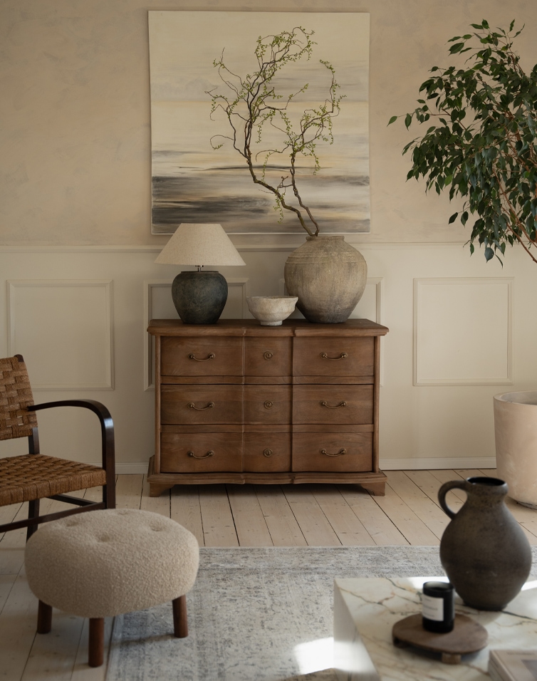 Cómoda de madera natural con seis cajones, jarrones decorativos y lámpara en sala de estar elegante