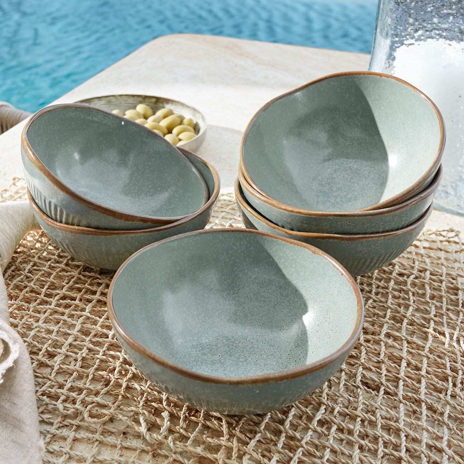 Set de 6 cuencos Périers Conjunto de cuencos de cerámica verde con borde marrón sobre un tapete natural en mesa exterior