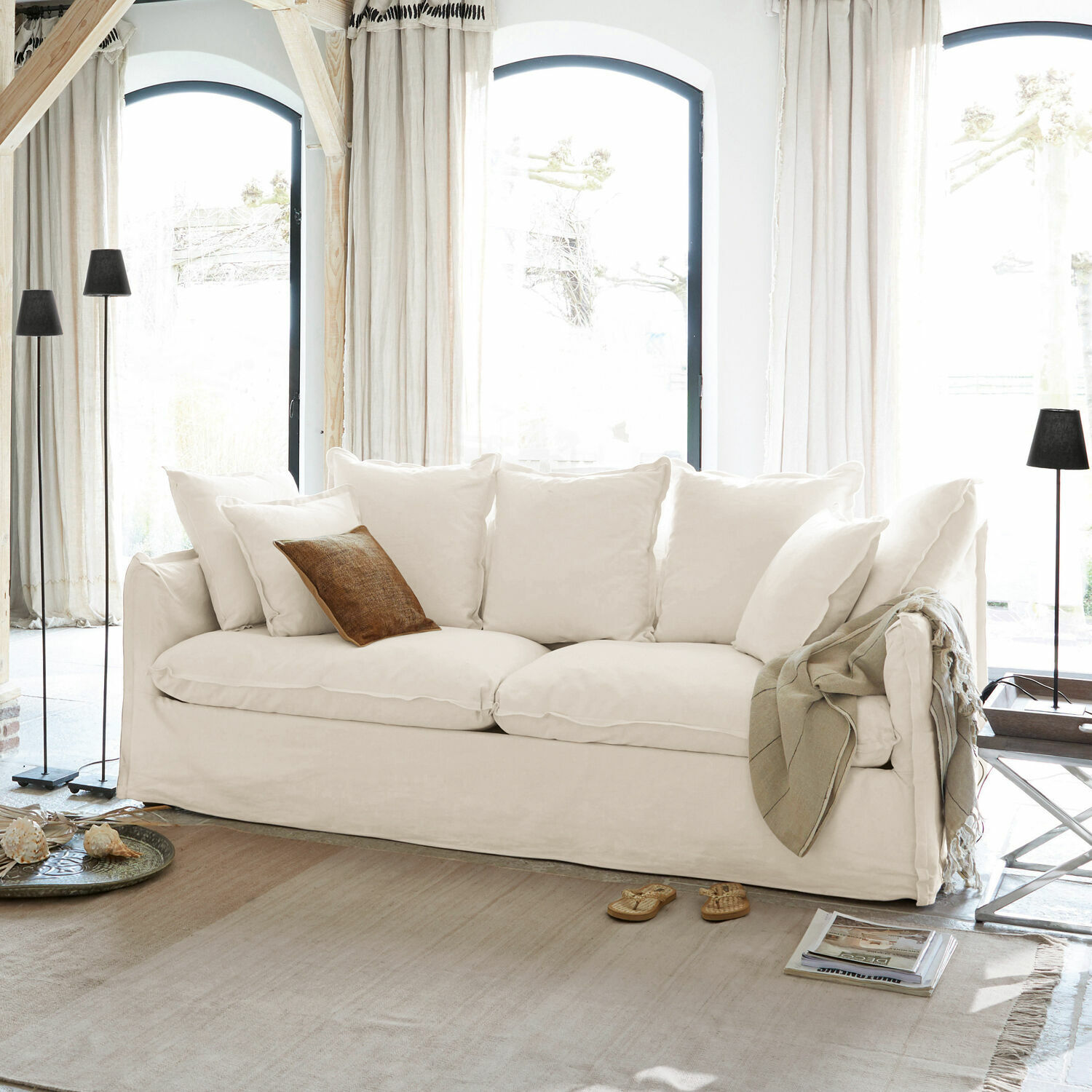 Sofá Tienen Sofá blanco con cojines suaves y cojín decorativo marrón en salón luminoso con grandes ventanas