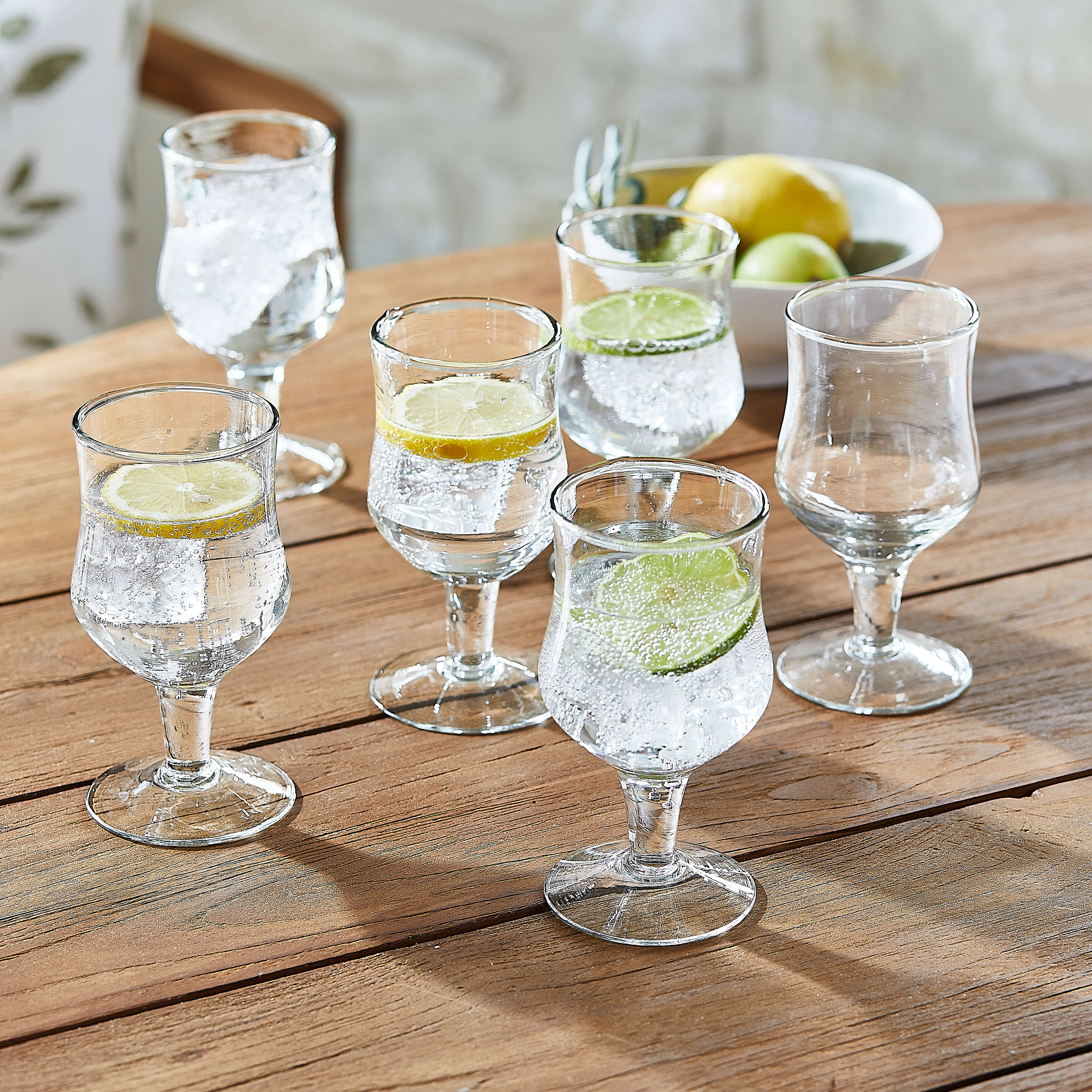 Conjunto de seis vasos transparentes con agua y rodajas de limón y lima sobre mesa de madera