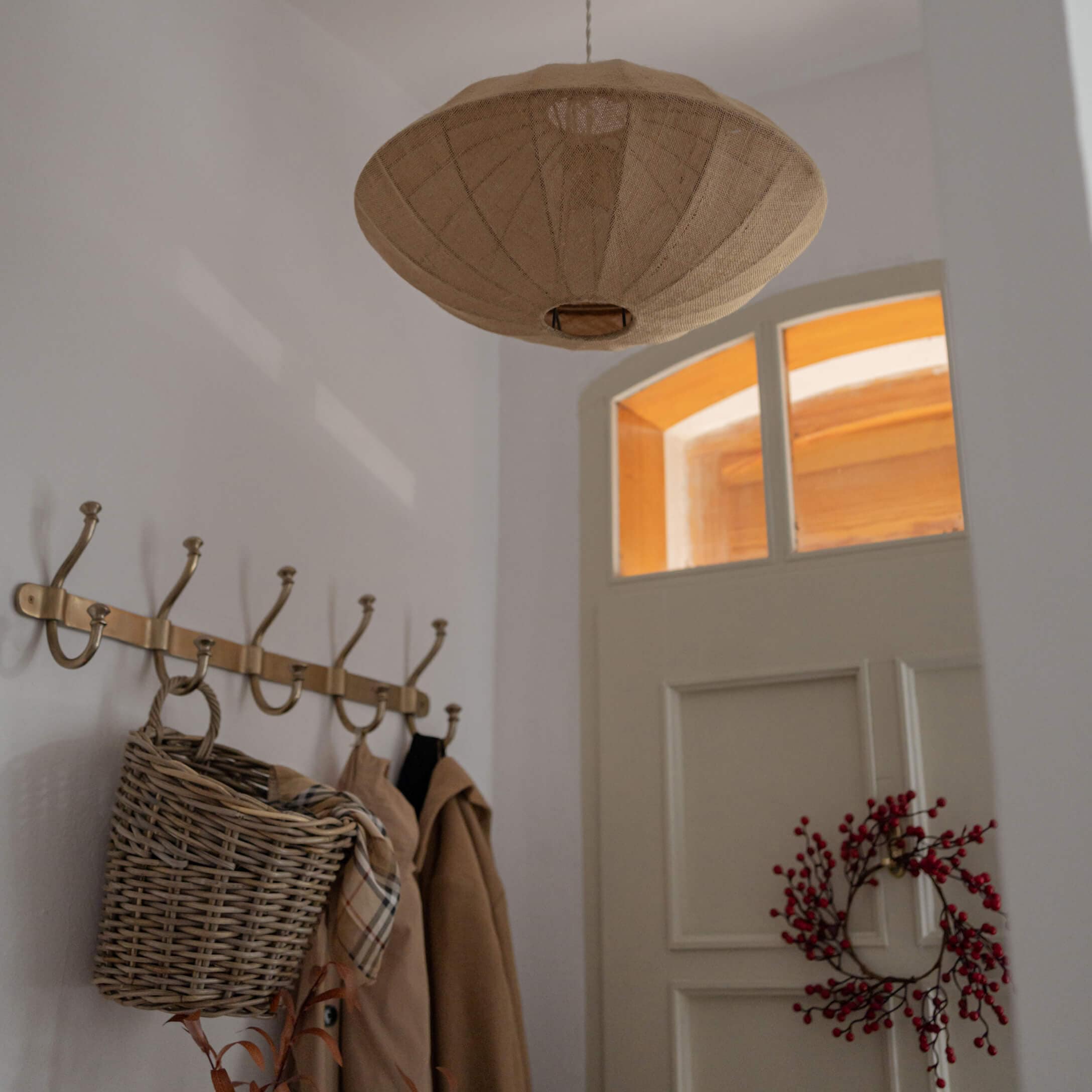 Lámpara colgante beige de tela con forma amplia en recibidor con perchero y cesta de mimbre