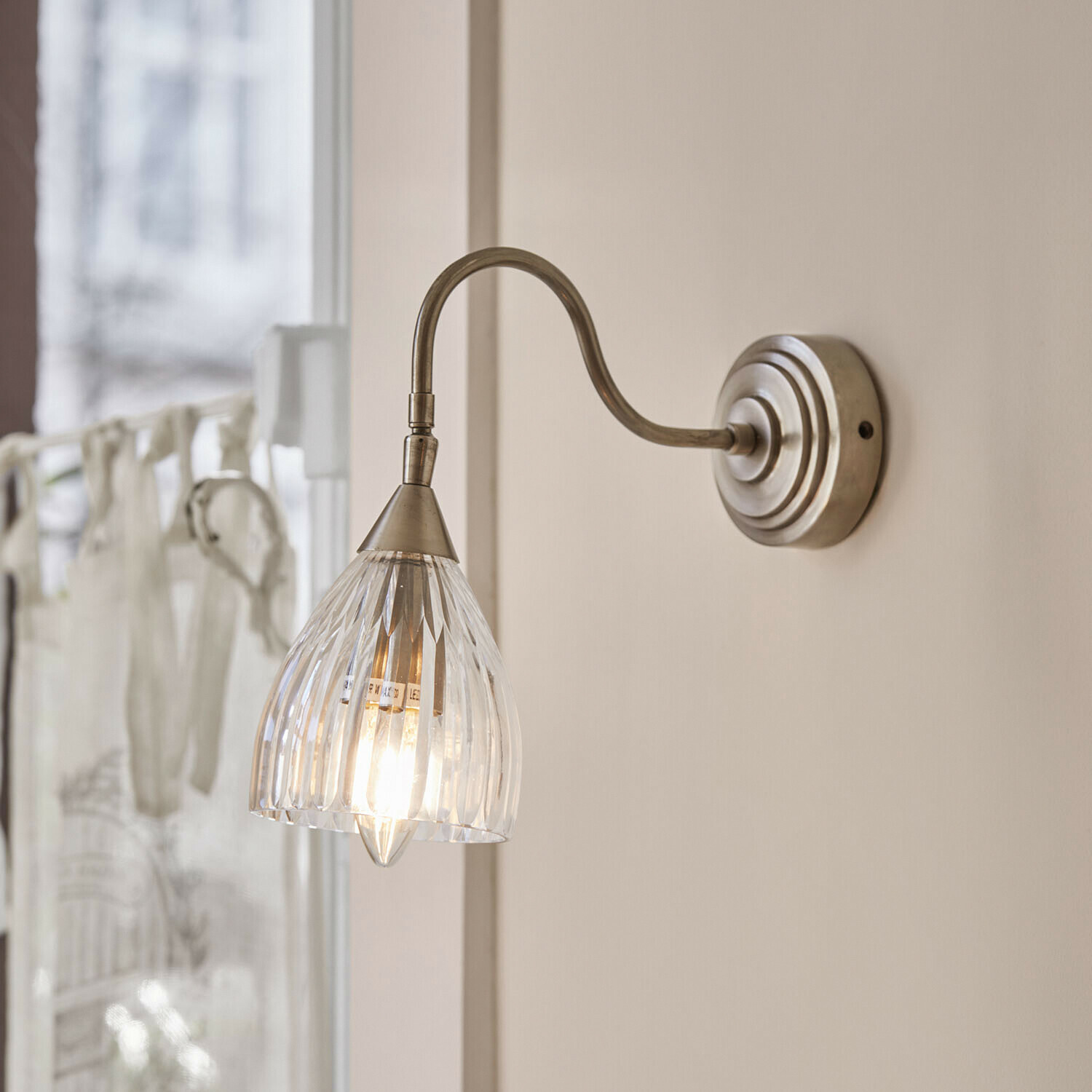 Lámpara de pared Niamhs Aplique de pared con pantalla de cristal transparente y brazo metálico en color plata envejecida