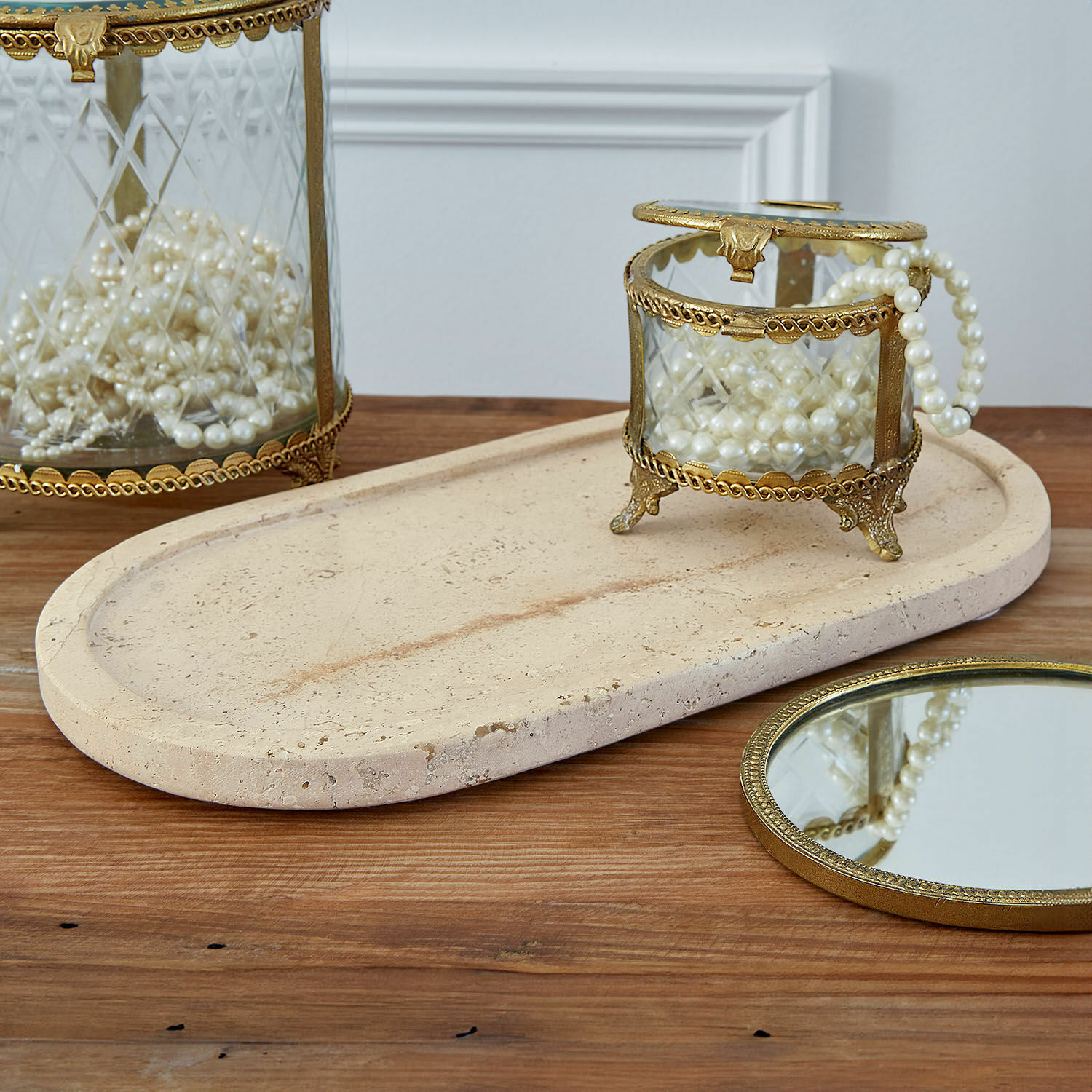 Caja de cristal con marco de latón y perlas sobre bandeja de piedra beige en mesa de madera