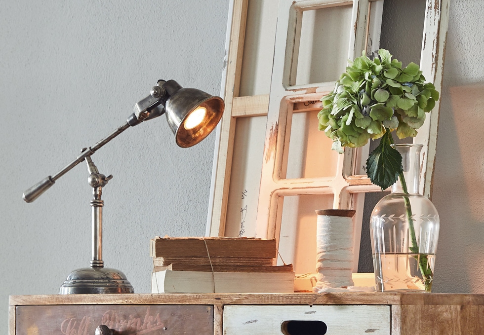 Lámpara de mesa metálica estilo industrial sobre mueble de madera con libros y jarrón con flor verde
