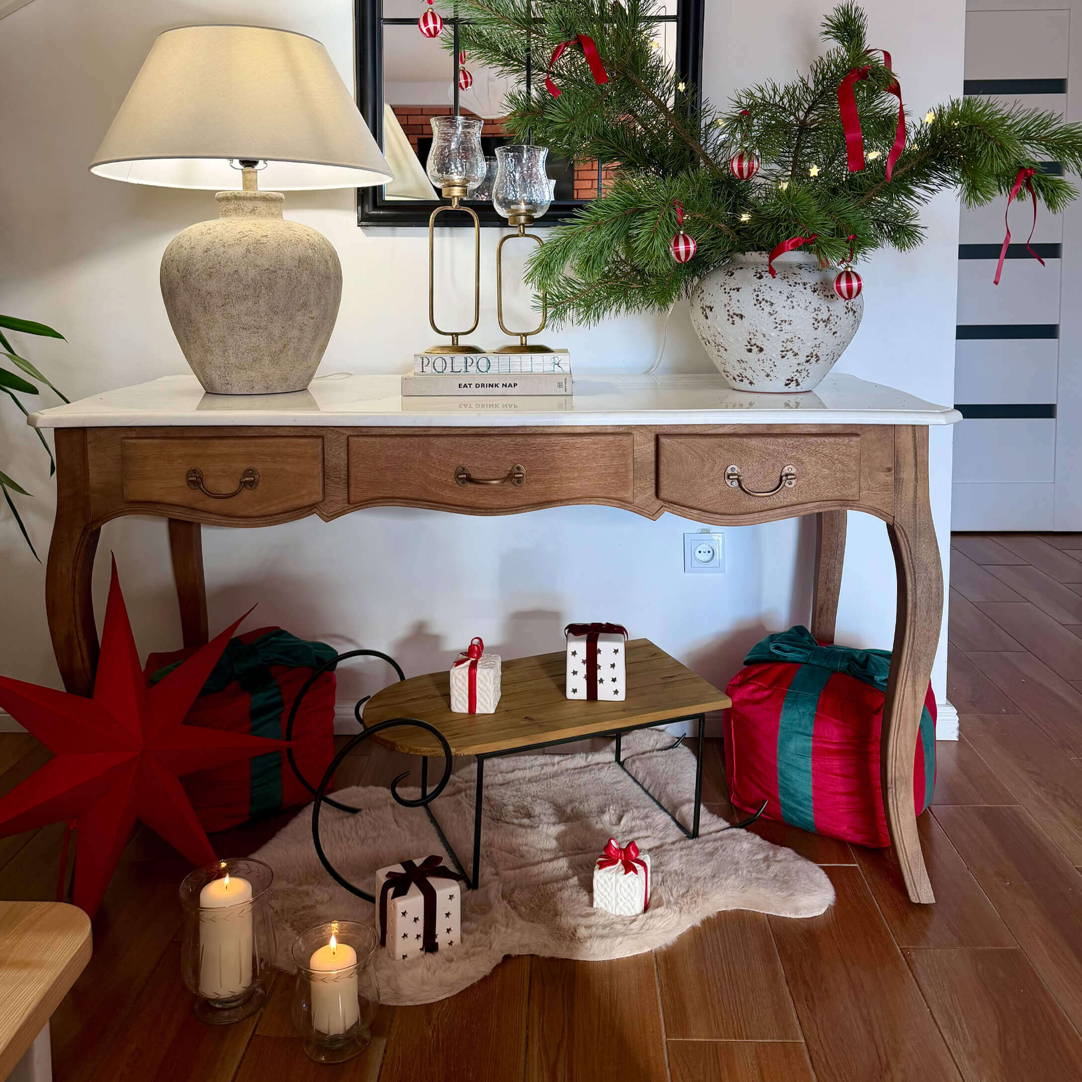 Mesa de madera con superficie blanca, lámpara y decoración navideña con ramas verdes y lazos rojos