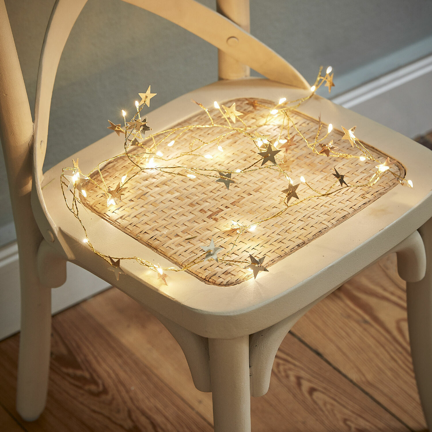 Cadena de luces con estrellas en luz cálida sobre asiento de mimbre claro