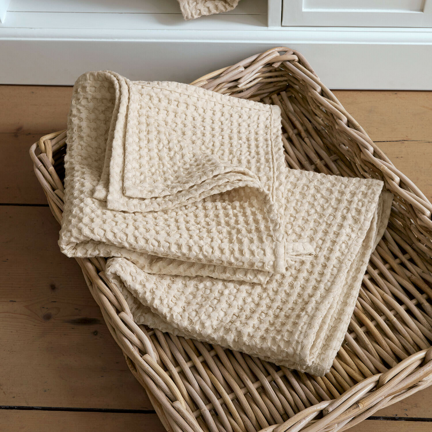 Set de 2 toallas Maralei Toalla beige de algodón con textura de gofre en cesta de mimbre sobre suelo de madera
