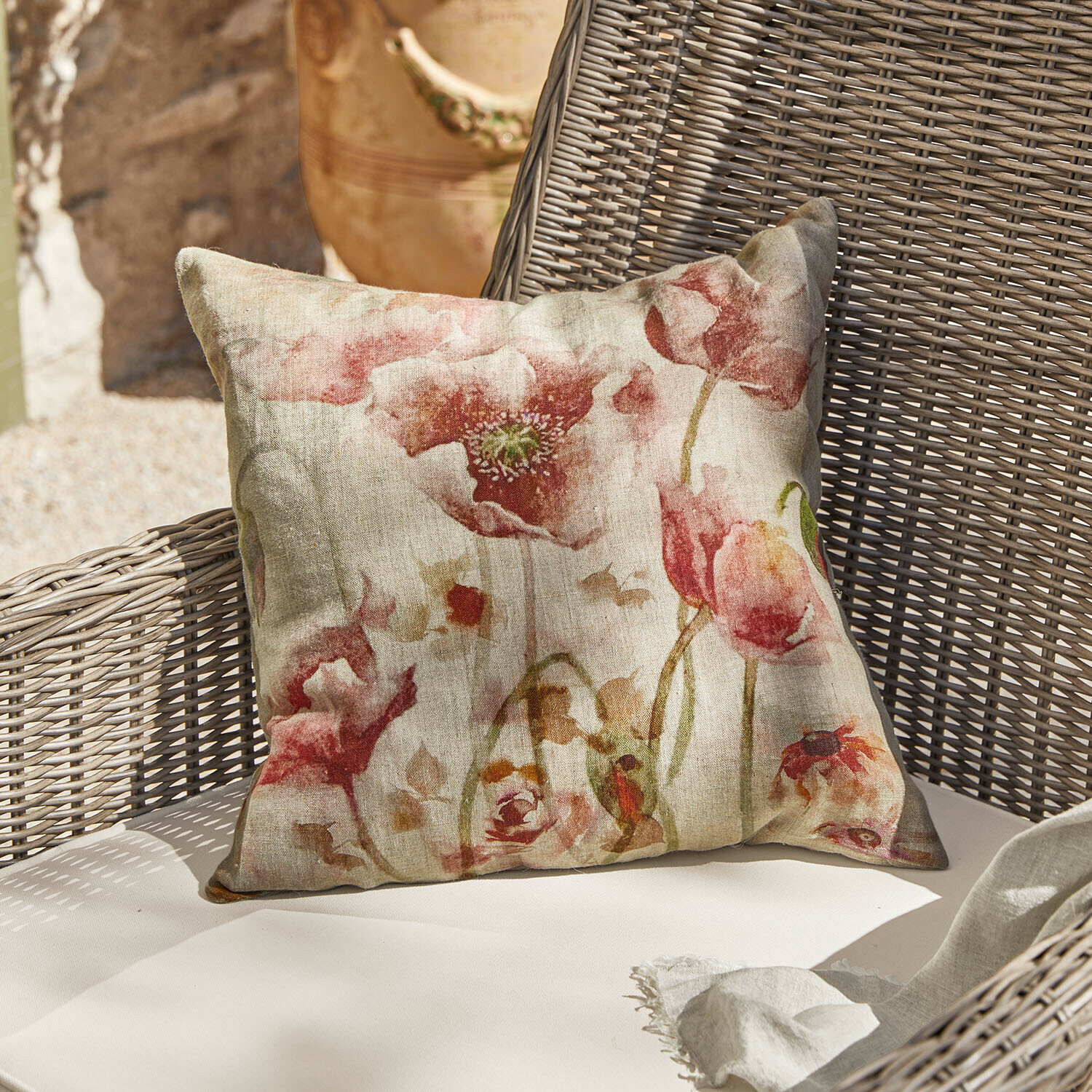 Funda de cojín Garavine Cojín decorativo de lino con estampado floral rojo sobre sillón de mimbre beige