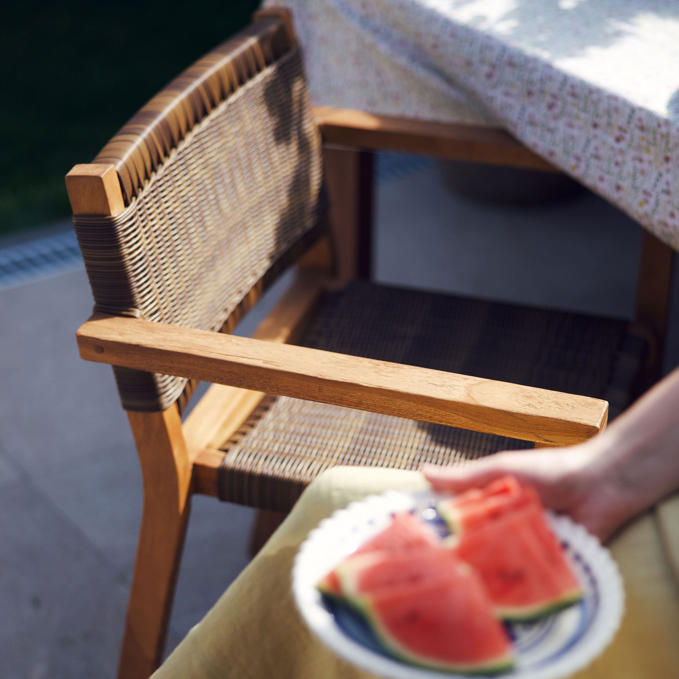 Silla de jardín de madera y mimbre natural junto a una mesa con mantel estampado
