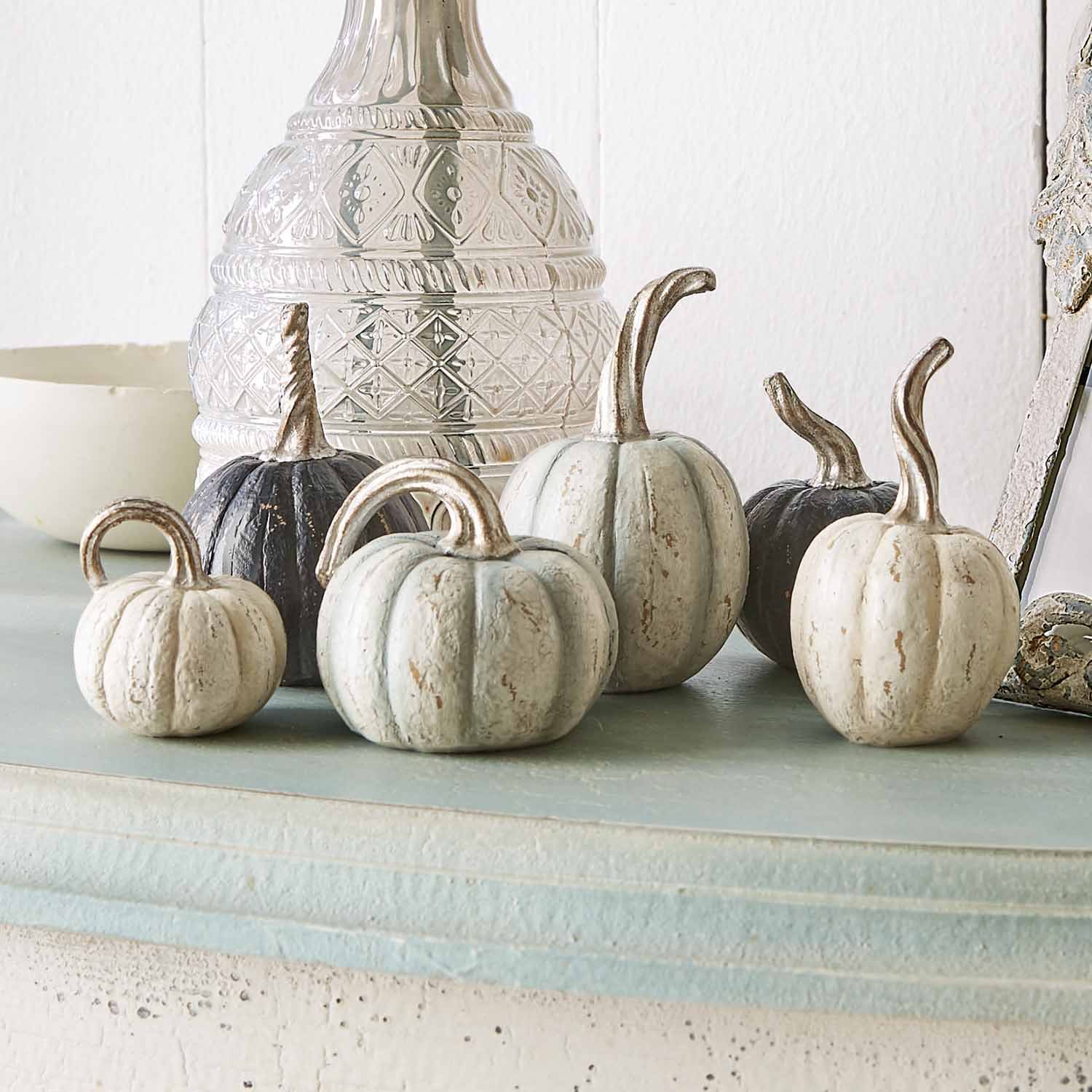 Calabazas decorativas de metal en blanco y negro sobre estante claro para decoración otoñal