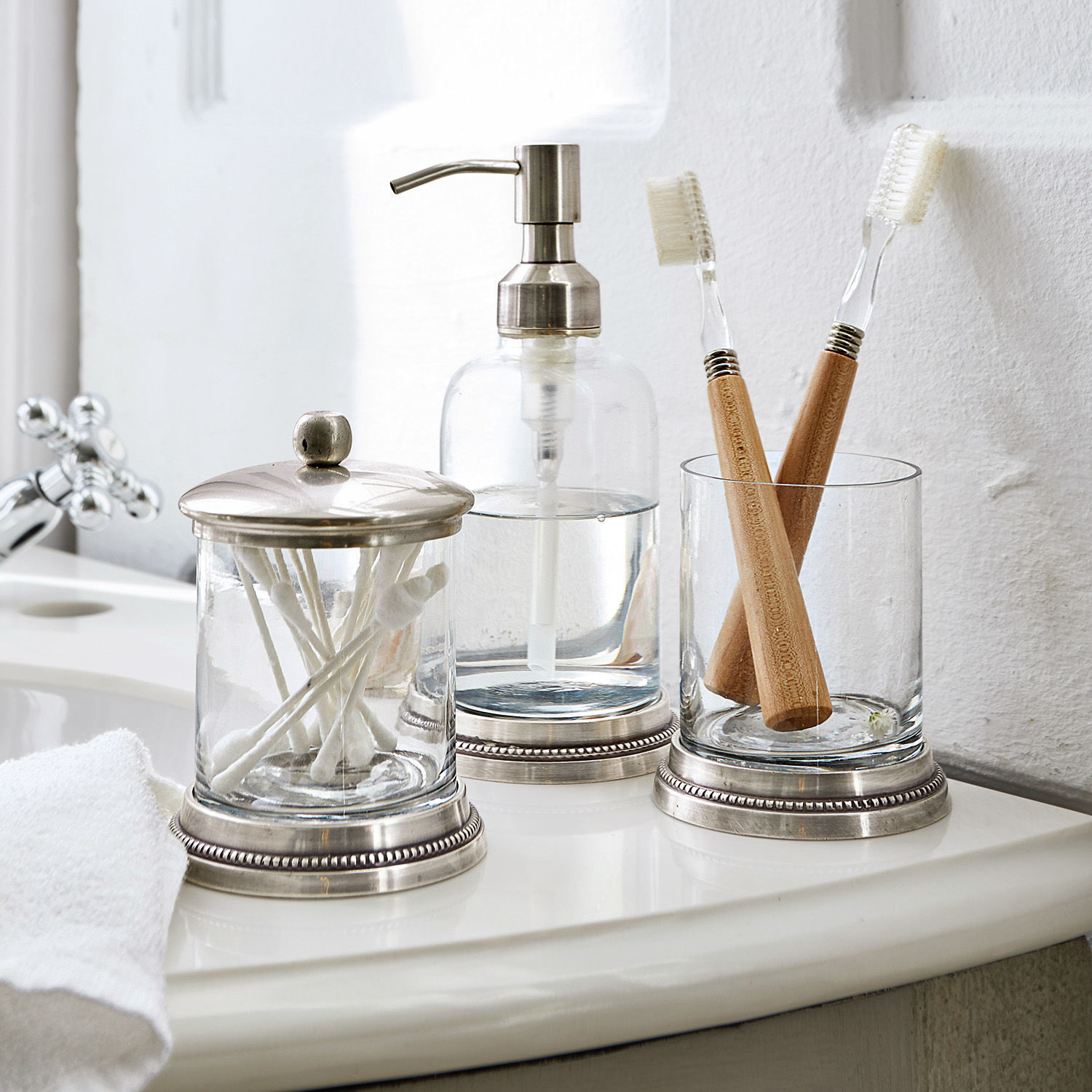 Set de baño Drinapoly Accesorios de baño de vidrio con detalles metálicos sobre lavabo blanco con cepillos de dientes de bambú