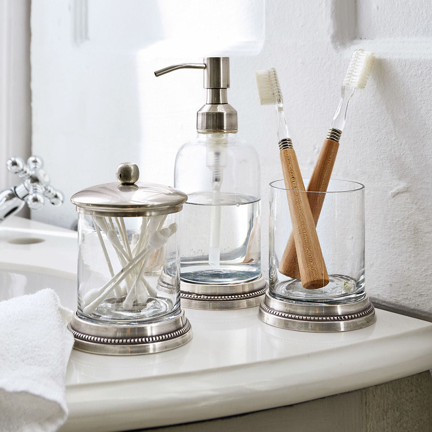 Set de baño Drinapoly Accesorios de baño de vidrio con detalles metálicos sobre lavabo blanco con cepillos de dientes de bambú