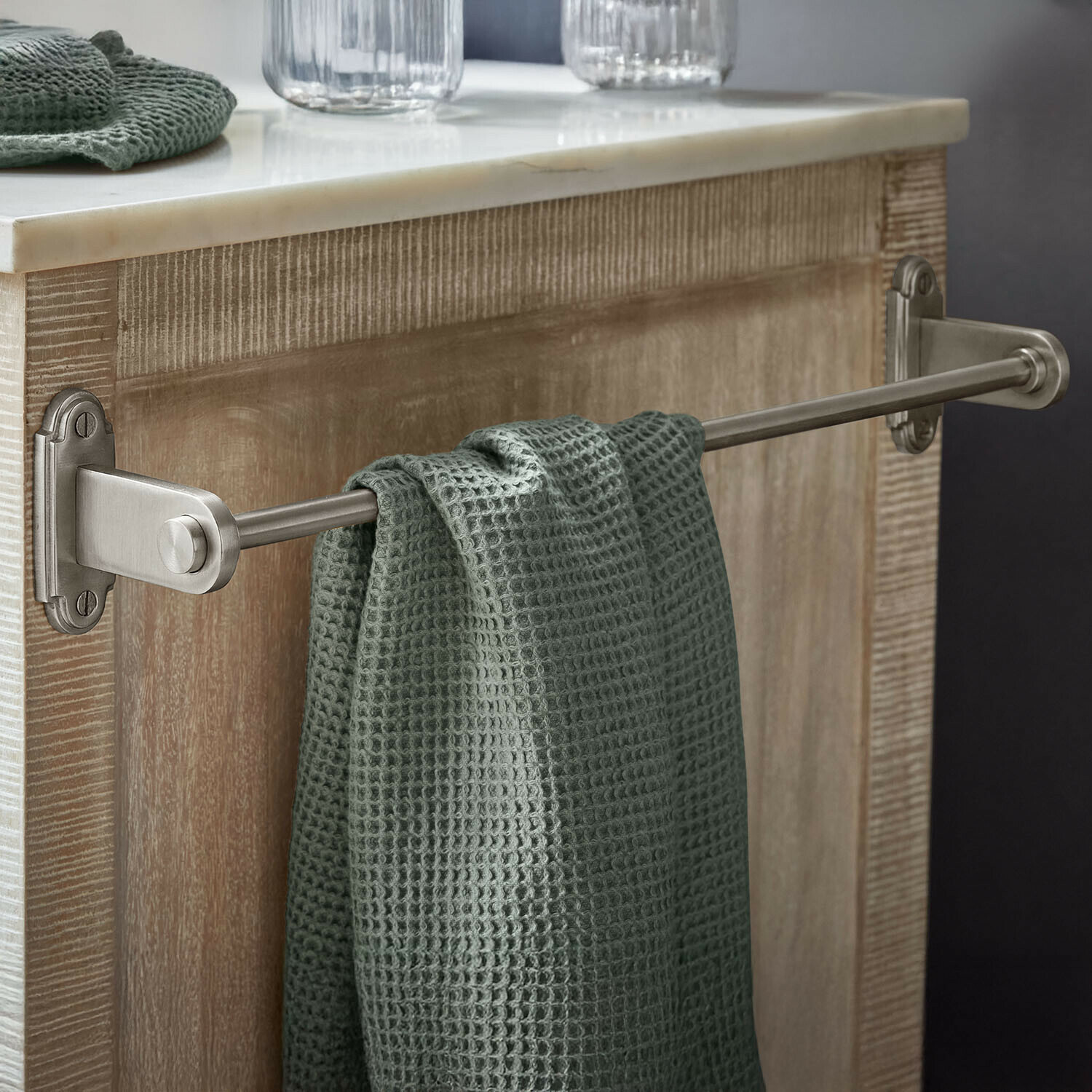 Toallero Virellane Toallero metálico con toalla verde de textura gofrada colgado en mueble de madera clara