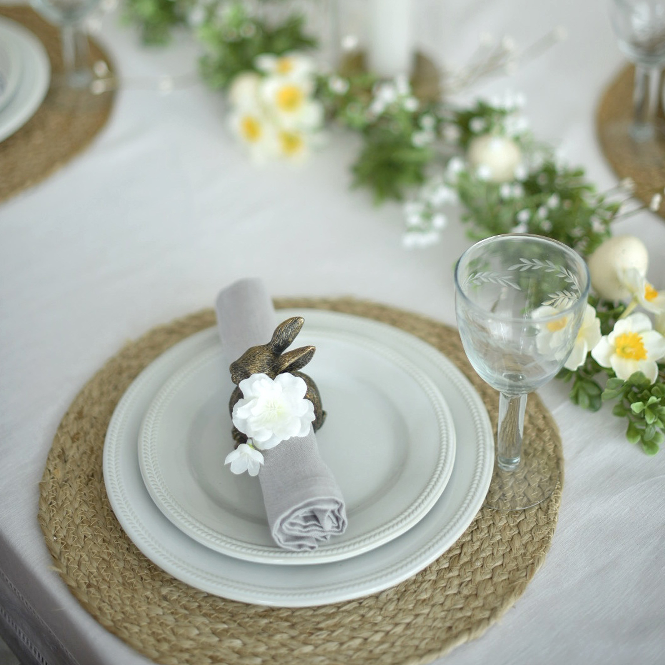 Vajilla blanca sobre base trenzada con servilletero de conejo y decoración floral delicada