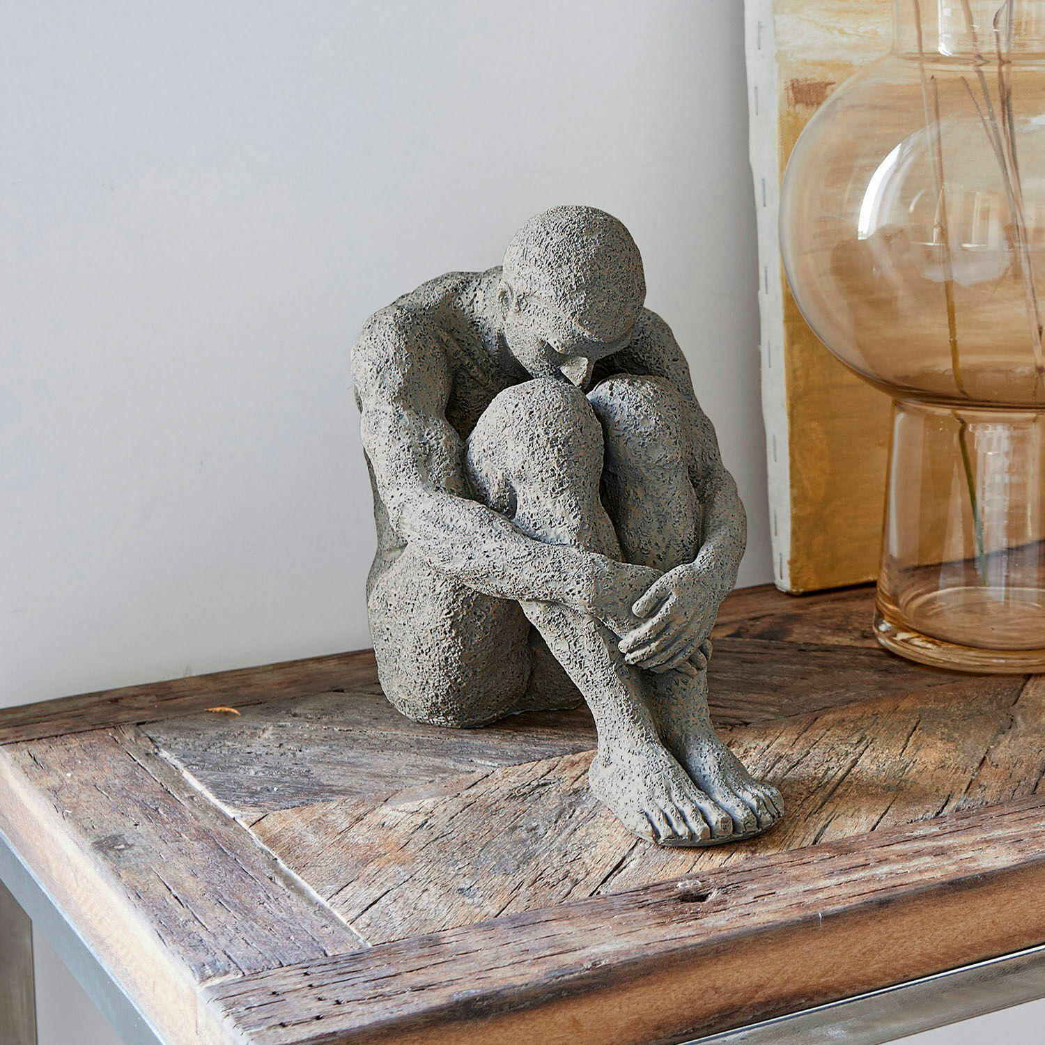 Escultura Antony Figura gris de piedra de persona sentada sobre mesa de madera, decoración de interiores