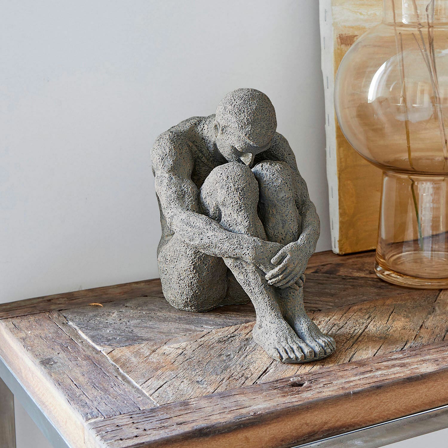 Escultura Antony Figura gris de piedra de persona sentada sobre mesa de madera, decoración de interiores