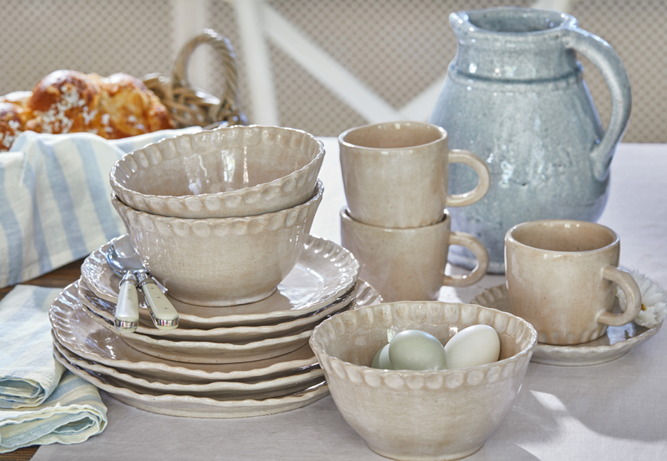 Juego de vajilla de cerámica beige con platos, cuencos y tazas sobre mesa rústica