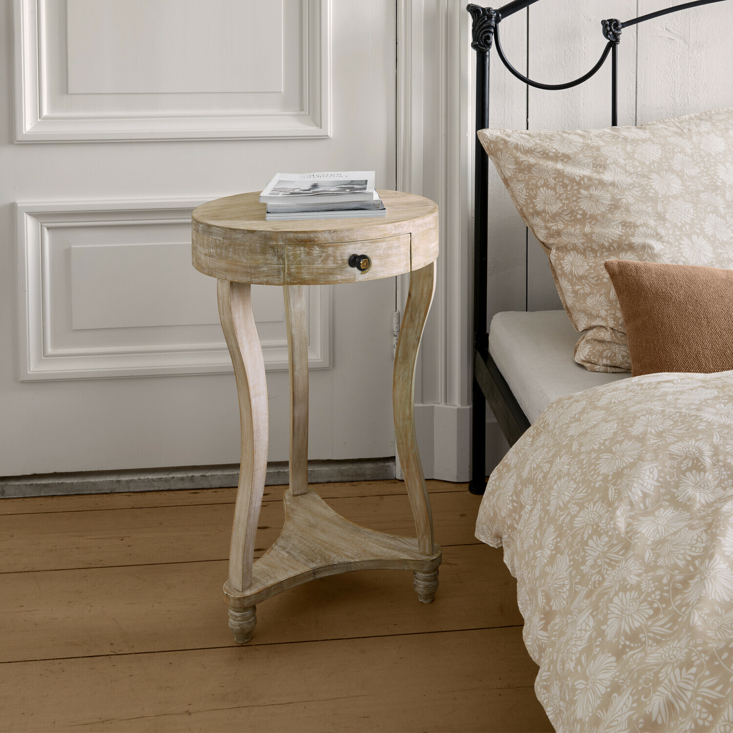 Mesa auxiliar Elmbury Mesa auxiliar redonda de madera clara con cajón junto a cama con ropa de cama beige con flores