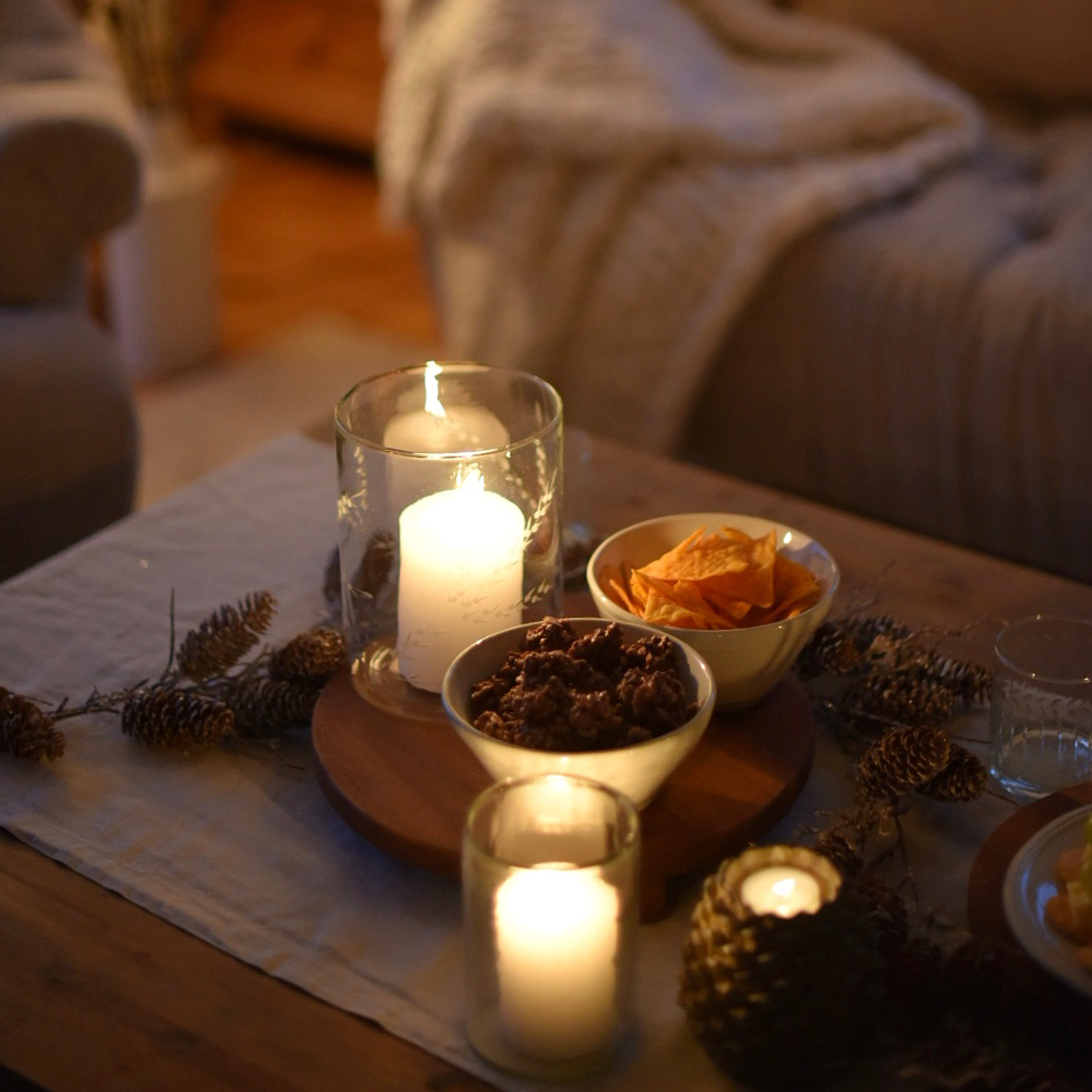 Velas en portavelas de vidrio y cuencos con aperitivos sobre mesa de madera en ambiente acogedor