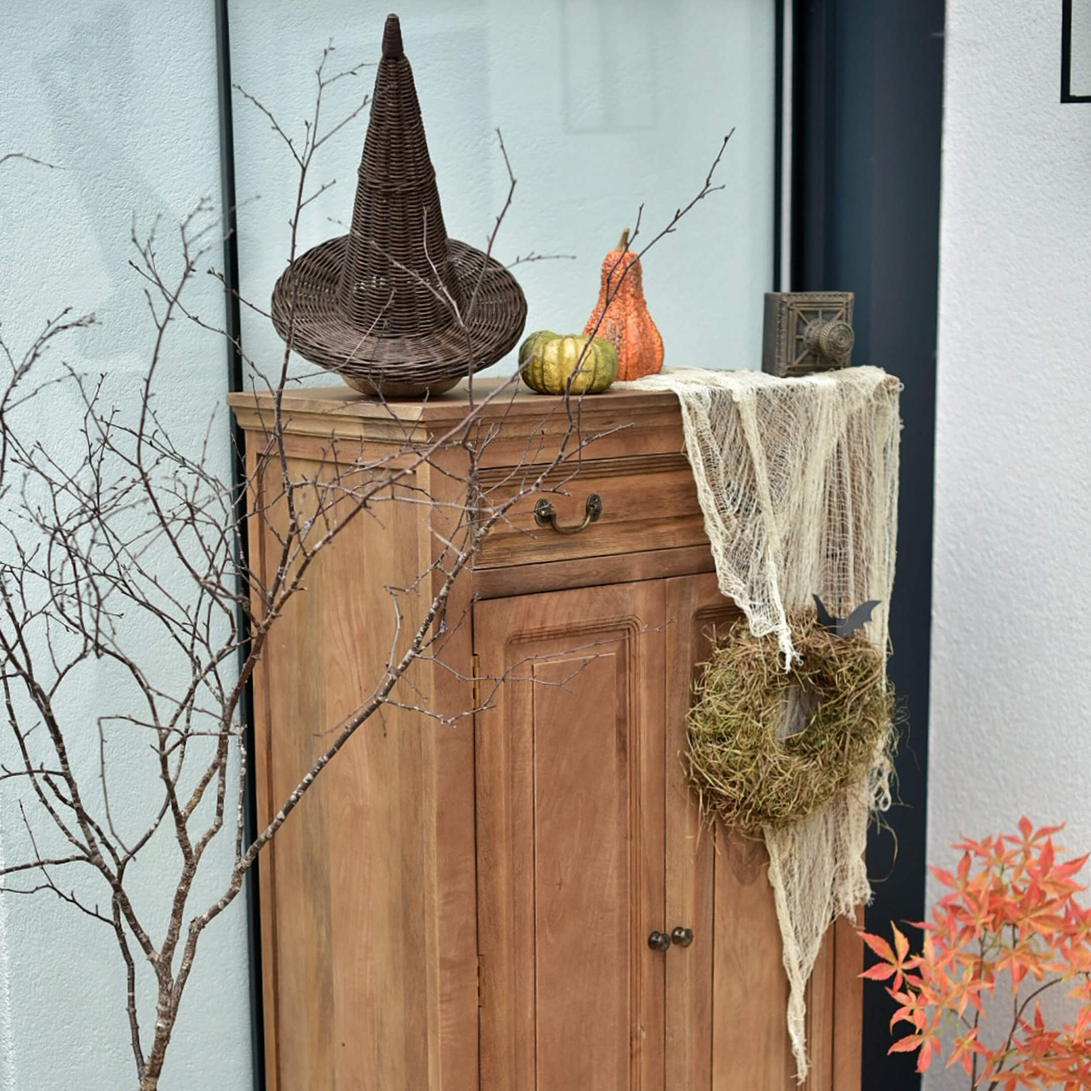 Armario de madera con decoración otoñal: sombrero de mimbre, calabazas y corona de musgo