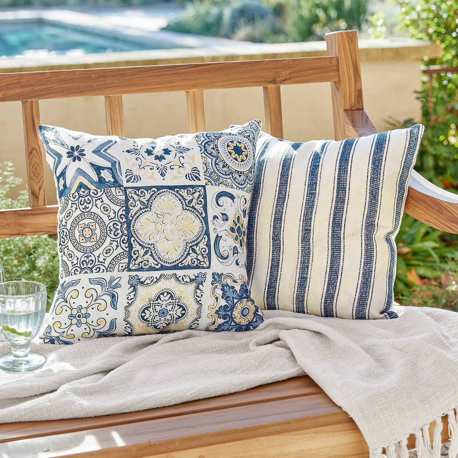 Set de 2 fundas de cojín Bourrignon Dos cojines decorativos de algodón con patrones azul y blanco sobre un banco de madera en el jardín