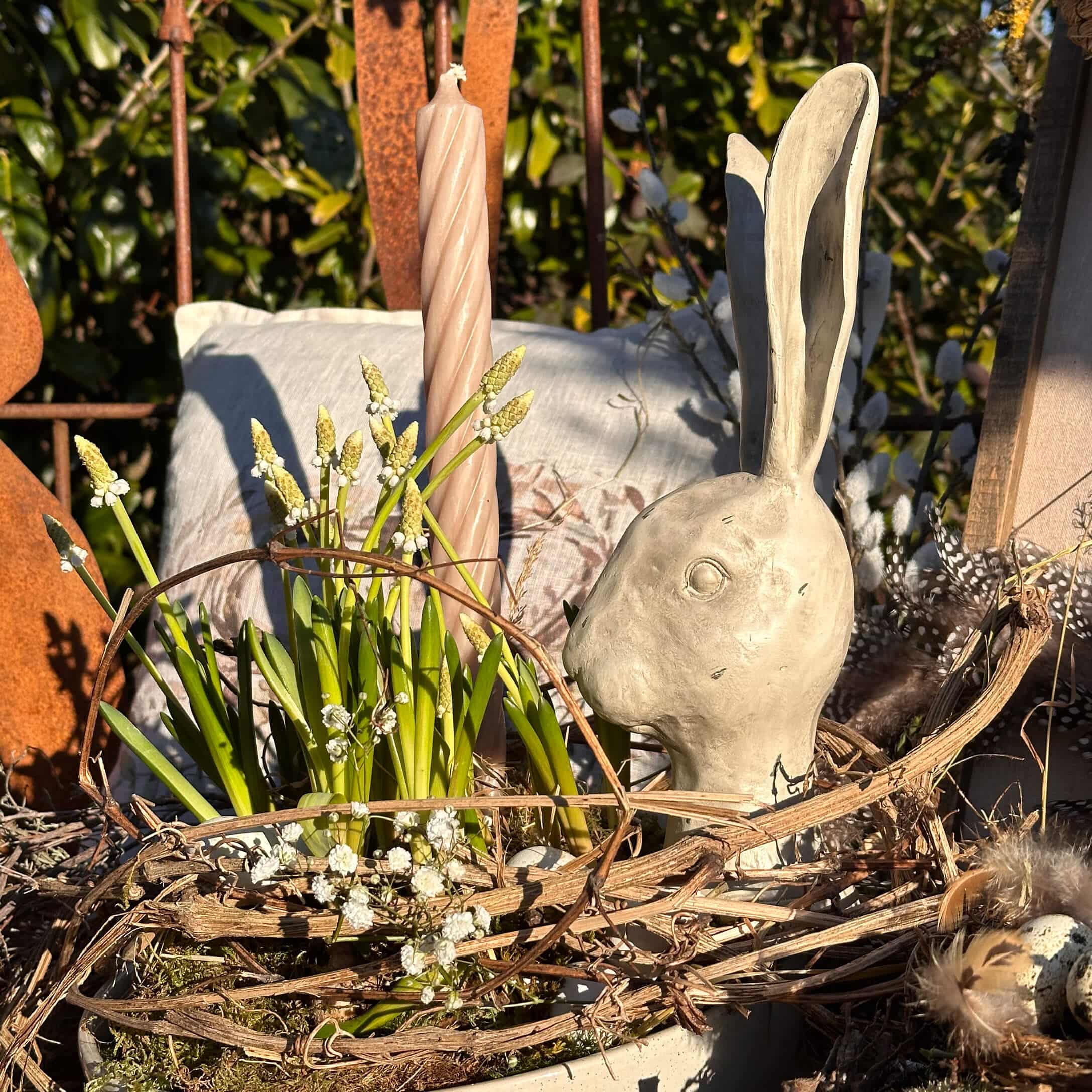 Decoración de Pascua con cabeza de conejo de cerámica gris y flores verdes en cesta natural