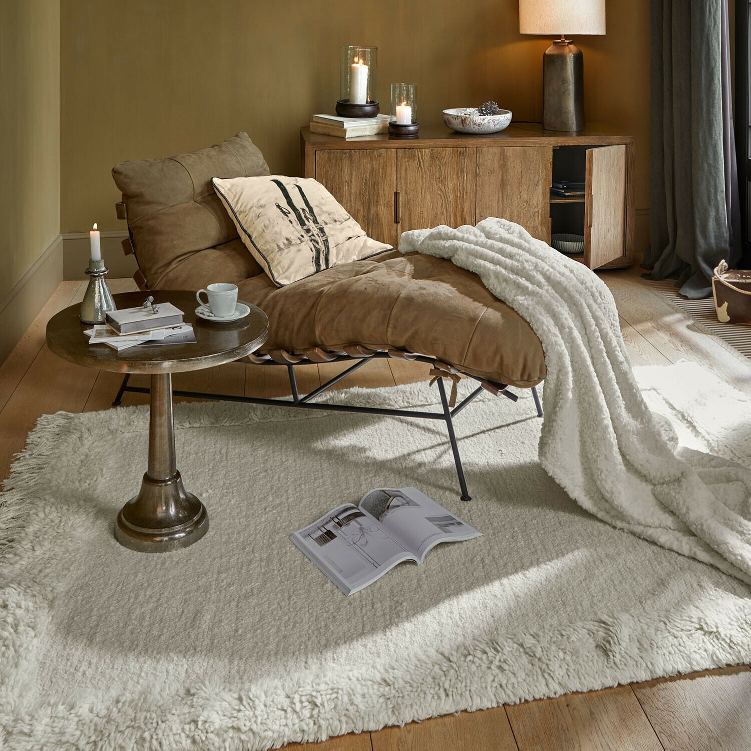 Sillón marrón de cuero con manta blanca sobre alfombra crema en sala acogedora