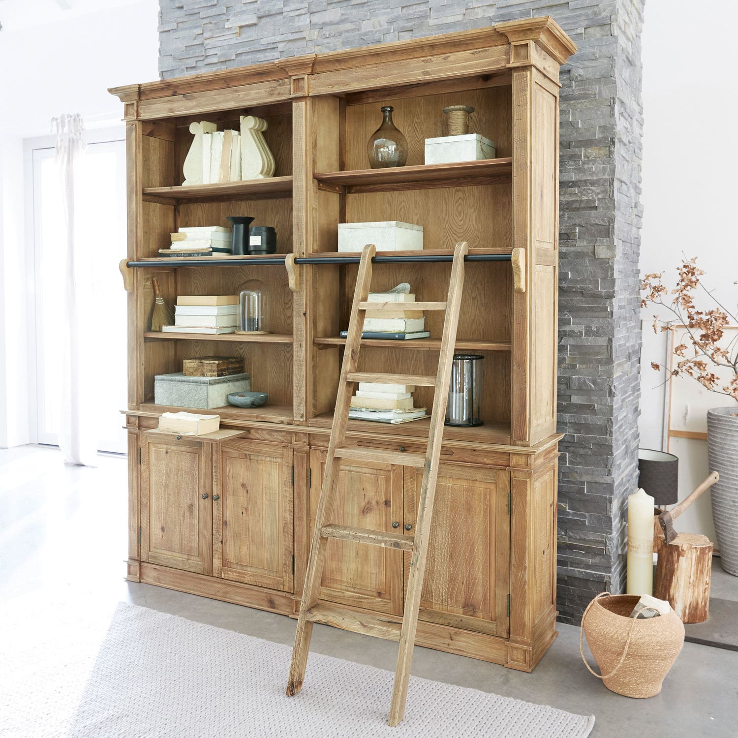 Librería Livera Gran estantería de madera con escalera y estantes llenos de libros y decoraciones en interior luminoso