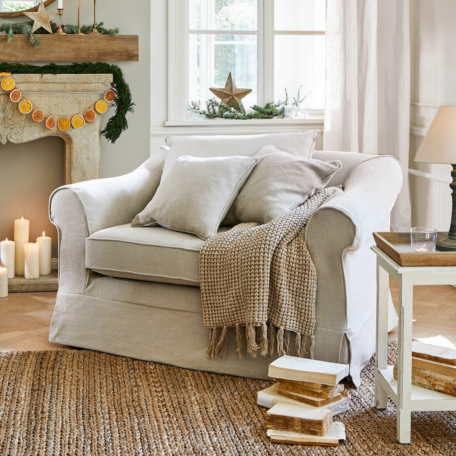 Sillón Folsom Sofá beige de tela con cojines y manta tejida sobre alfombra de yute en salón acogedor