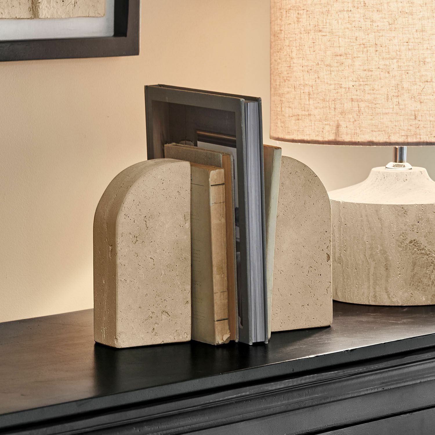 Sujetalibros de piedra beige con forma redondeada sobre estante negro en sala de estar