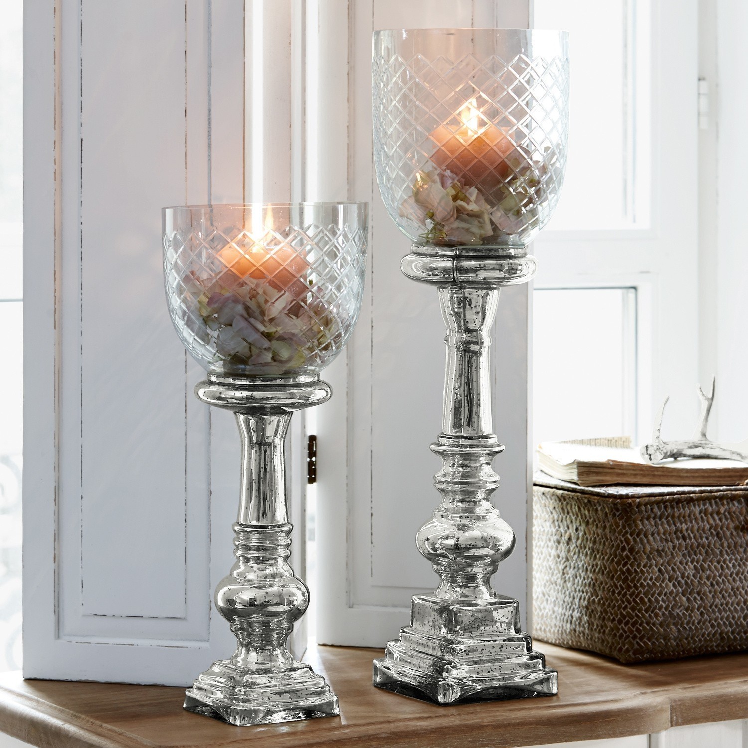 Set de 2 candeleros Layci Dos candelabros plateados con pantallas de vidrio y flores, decoración interior sobre mesa de madera