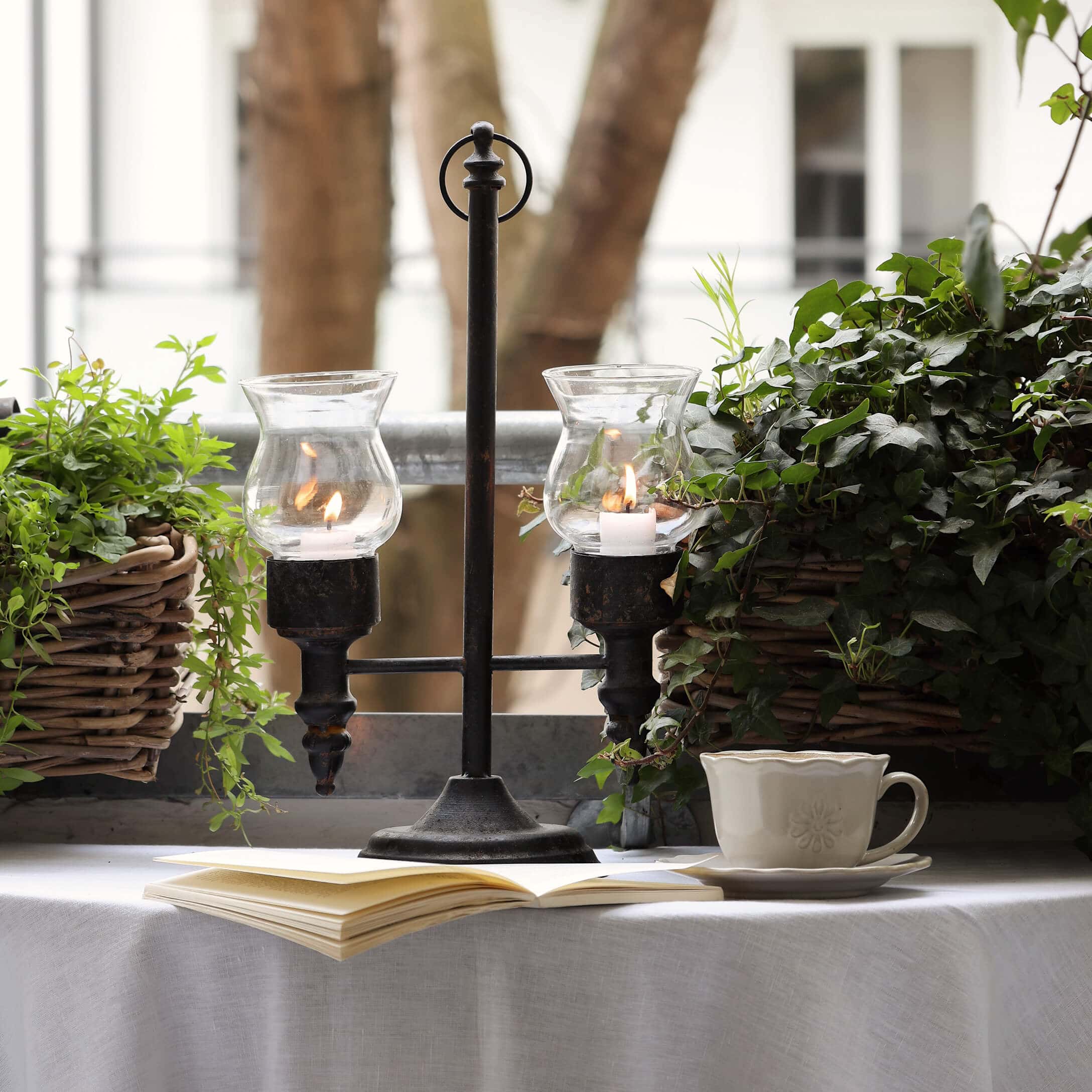 Candelabro de metal con dos protectores de vidrio entre plantas verdes en balcón